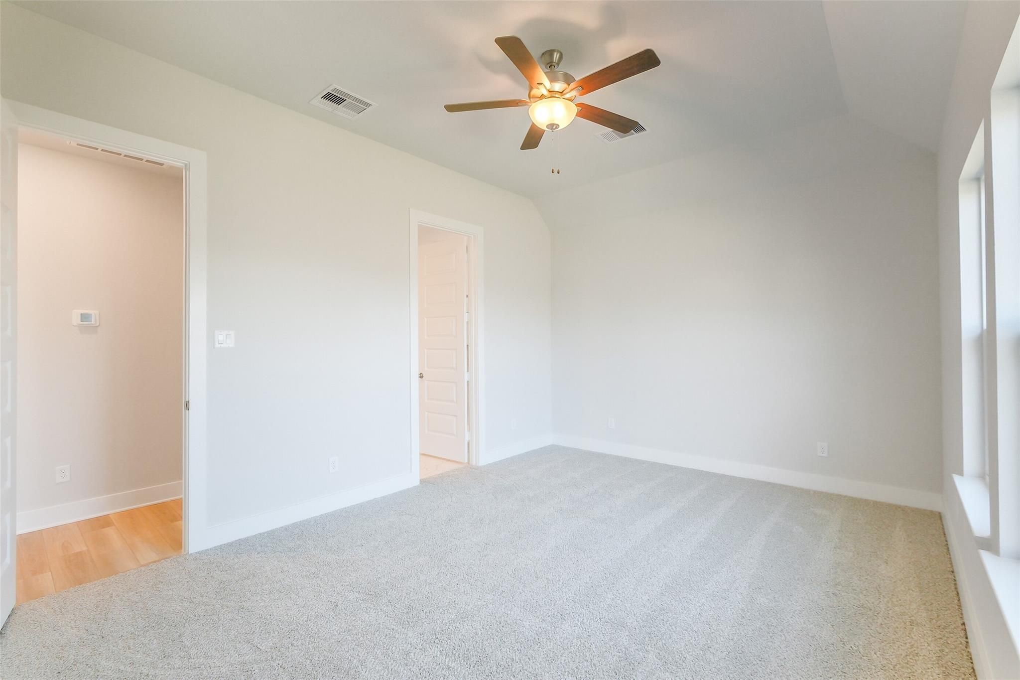 Spacious carpeted bedroom with ceiling fan, large windows, and open door to hardwood hallway in Davidson Homes The Luna L, Katy, Texas