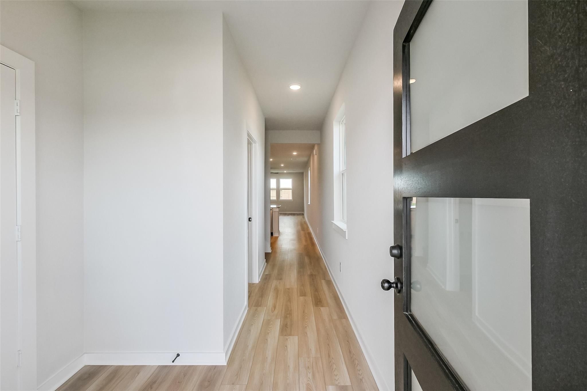 Bright hallway with light wood floors, white walls, and modern frosted glass door in 5-bedroom Davidson Homes San Marcos E, Beasley, Texas