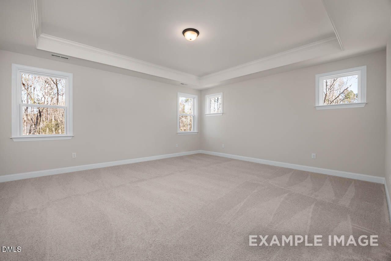 Spacious empty upstairs bedroom with tray ceiling, large windows overlooking trees, and neutral gray walls in Davidson Homes The Crawford D, Angier, NC