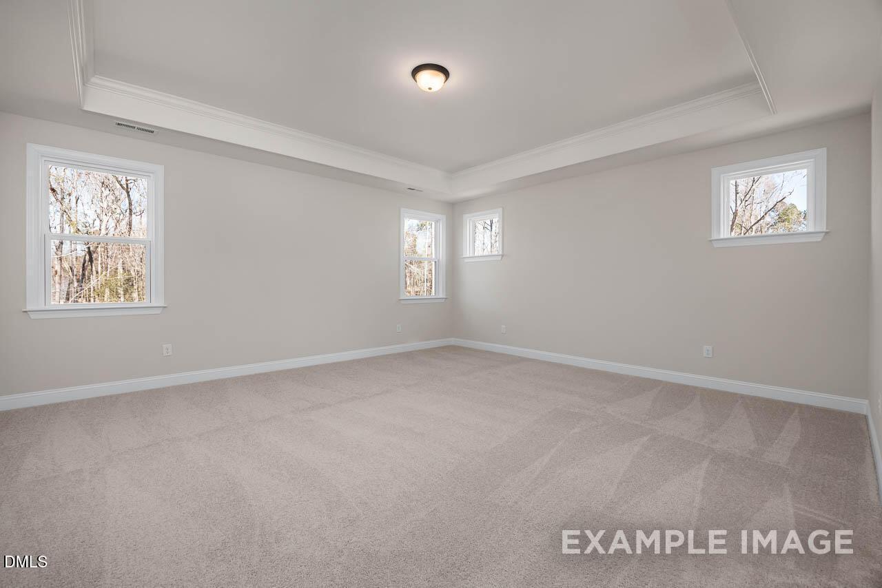 Spacious empty upstairs bedroom with tray ceiling, large windows overlooking trees, and neutral gray walls in Davidson Homes The Crawford D, Angier, NC