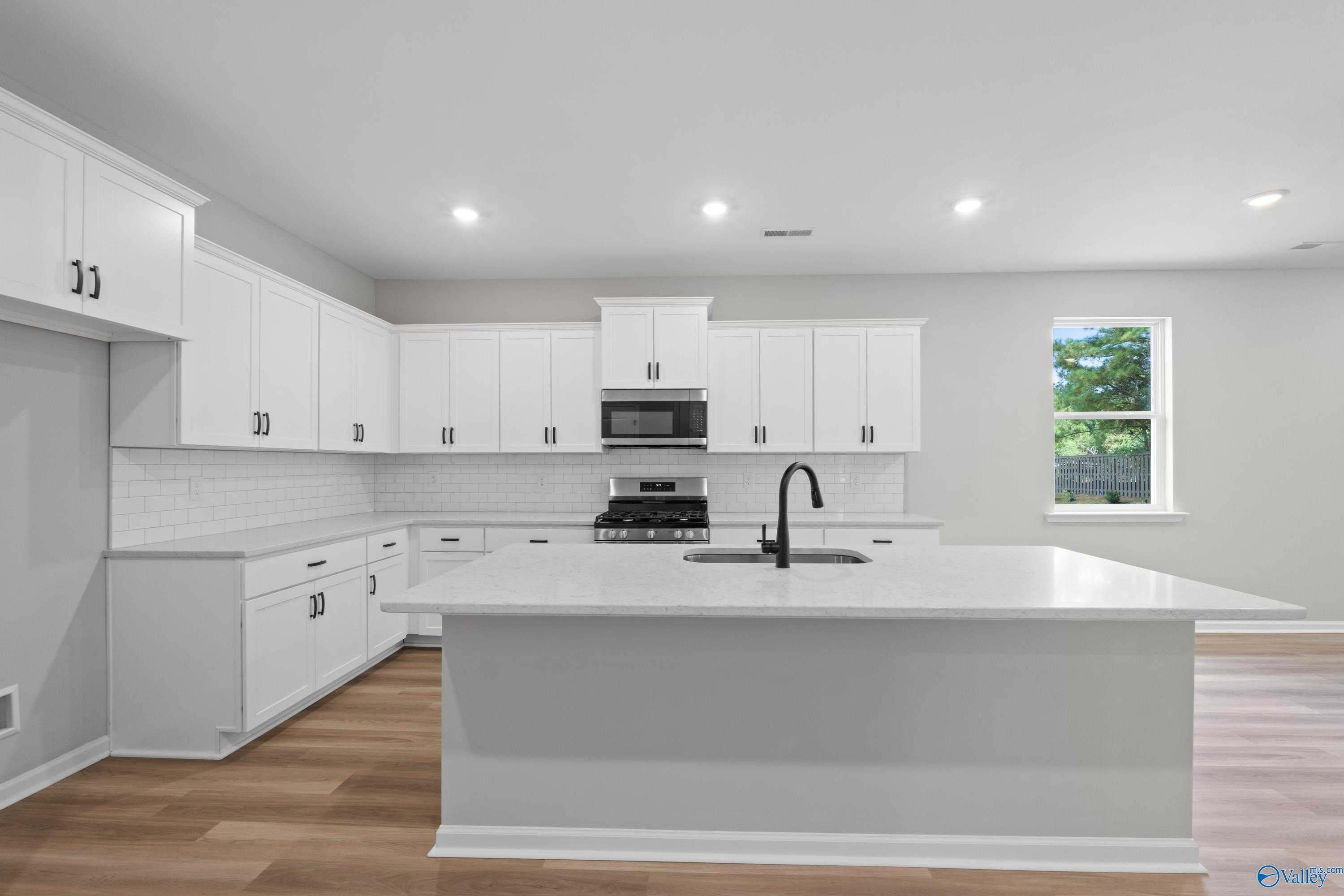 Modern white kitchen with large island sink, subway tile backsplash, and stainless appliances in Evermore Homes The Nantucket, Madison, AL