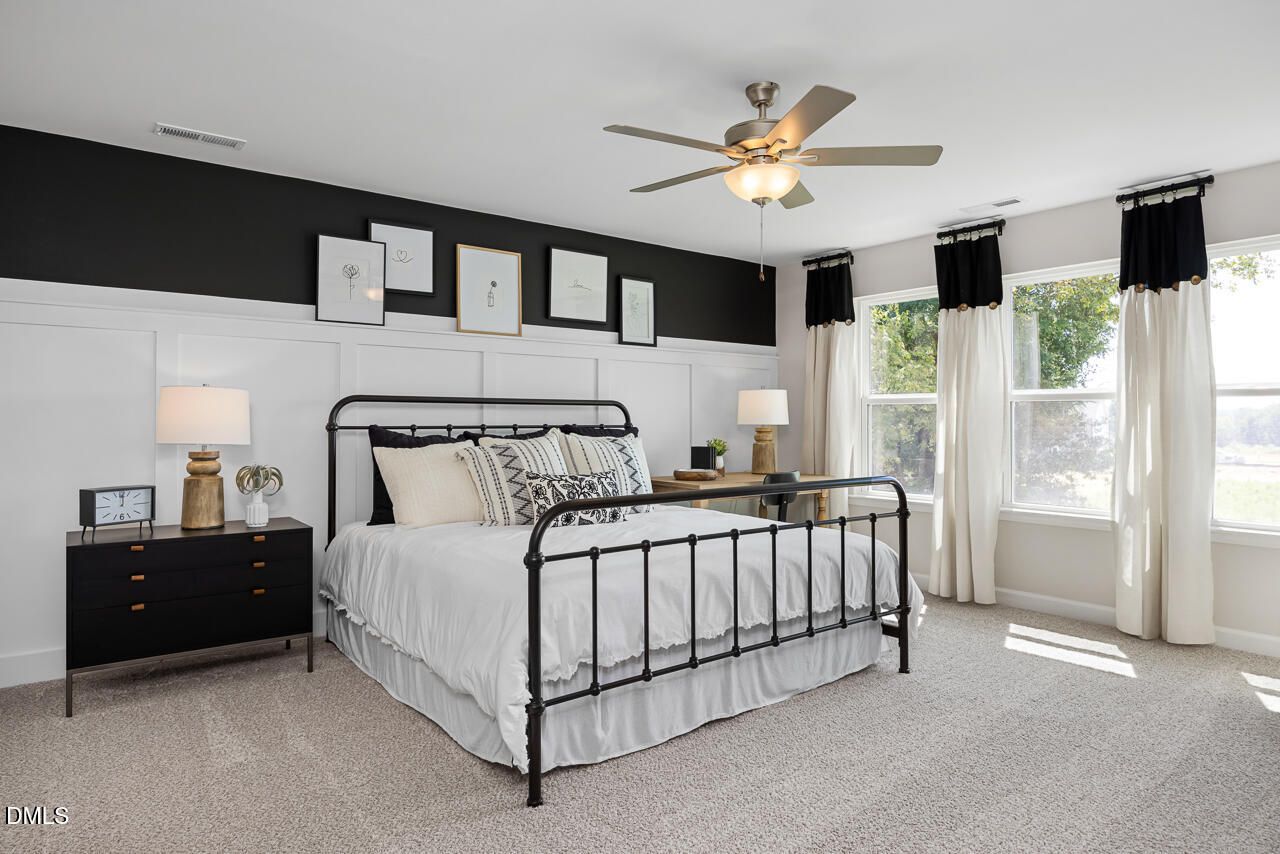 Elegant master bedroom with black iron bed, white linens, ceiling fan, and large windows in Davidson Homes The Hickory II C, Zebulon, NC