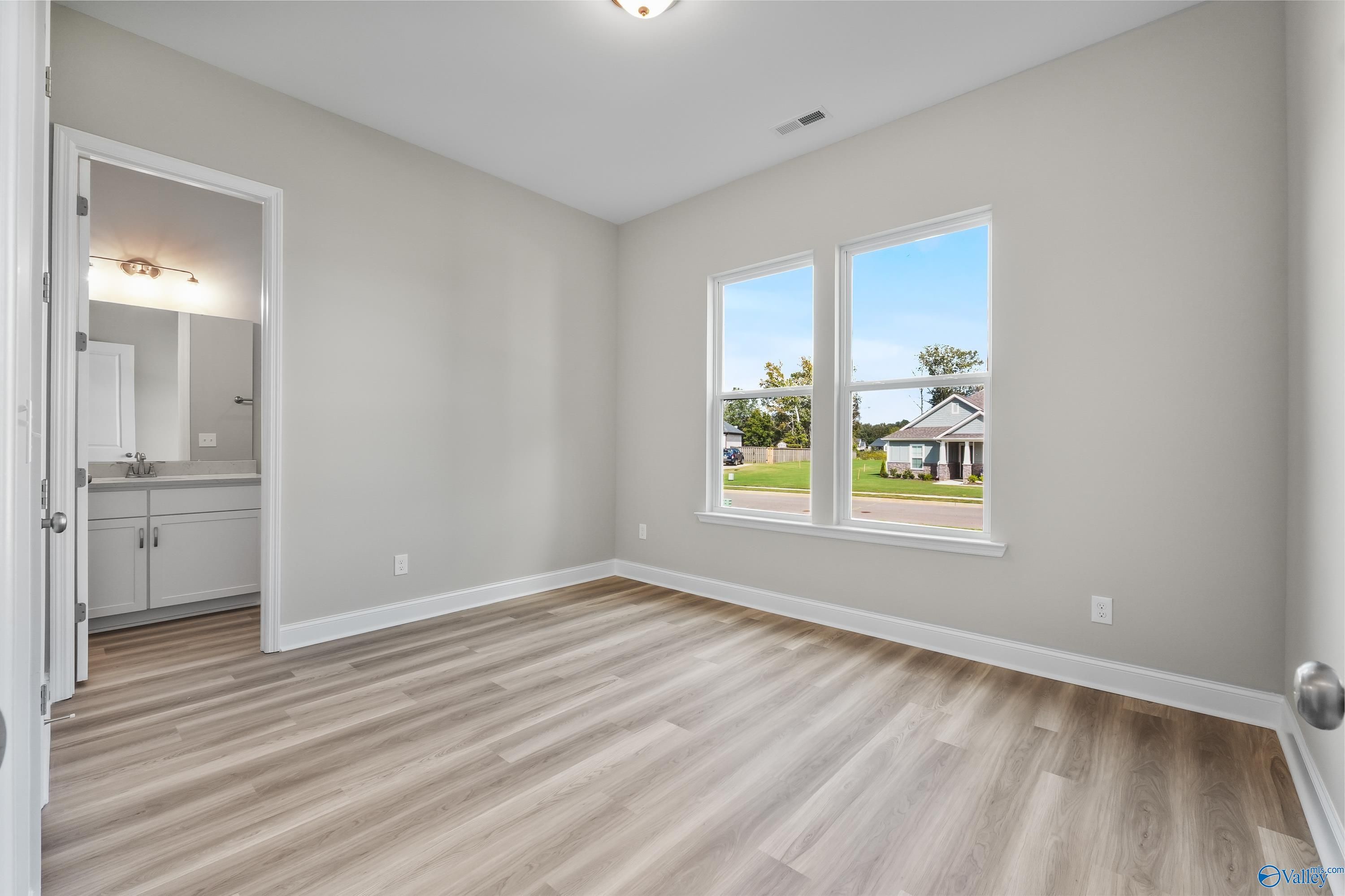 Bright secondary bedroom with en-suite bath, light gray walls, LVP flooring, and large windows overlooking green space in Evermore Homes The Haven, Owens Cross Roads, AL