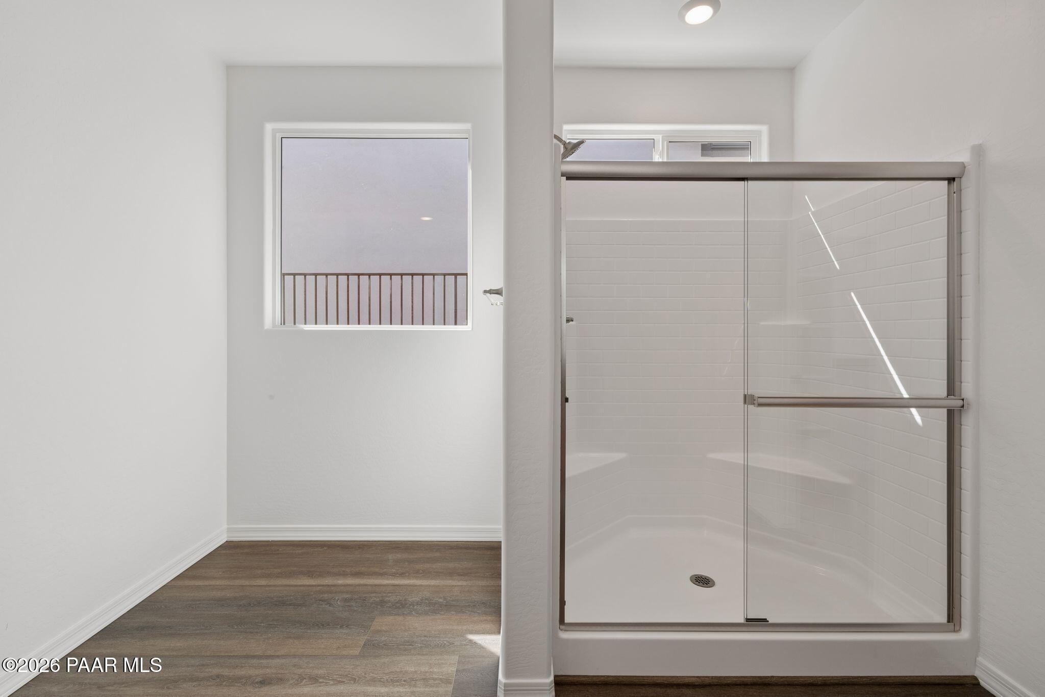 Modern master bathroom with frameless glass walk-in shower, window to balcony, and wood flooring in Davidson Homes The Monarch A, Prescott, Arizona