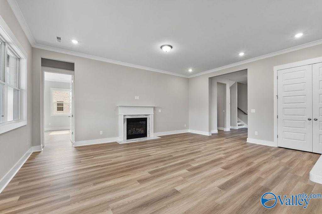 Spacious living room with gas fireplace, light hardwood floors, and open doorways in Evermore Homes The Oxford, Owens Cross Roads, AL