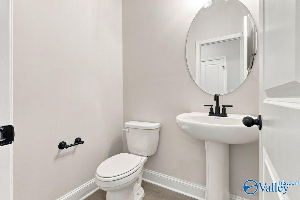 Elegant half bath with pedestal sink, oval mirror, and matte black fixtures in Davidson Homes Rockford plan, Hartselle, Alabama