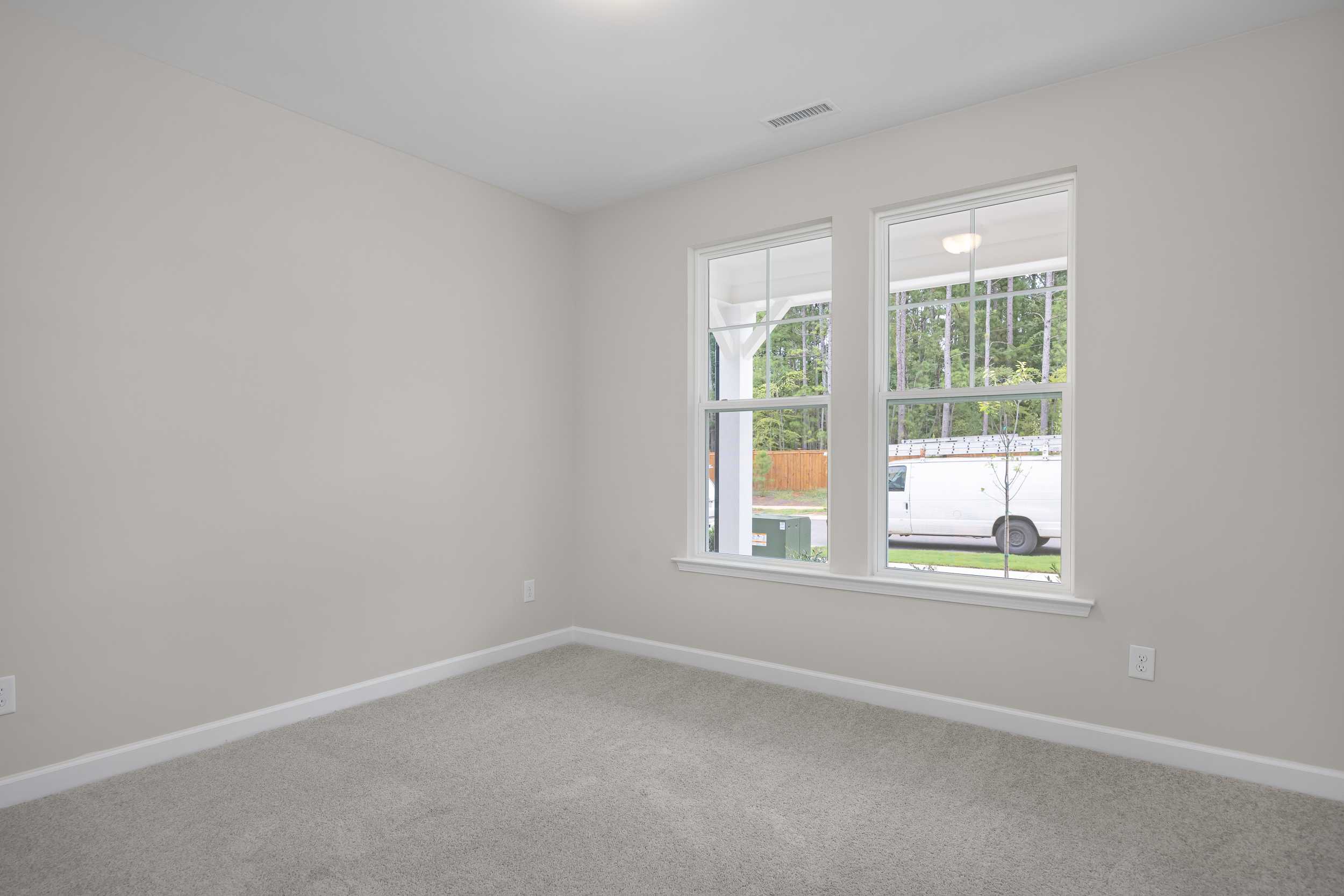 Spacious secondary bedroom in The Beech C with beige walls, gray carpet, large white-framed windows, and wooded view