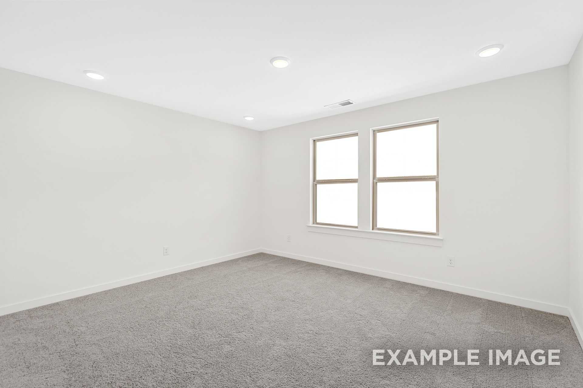 Bright upstairs bedroom in The Logan B with white walls, double casement windows, recessed lights, and gray carpet