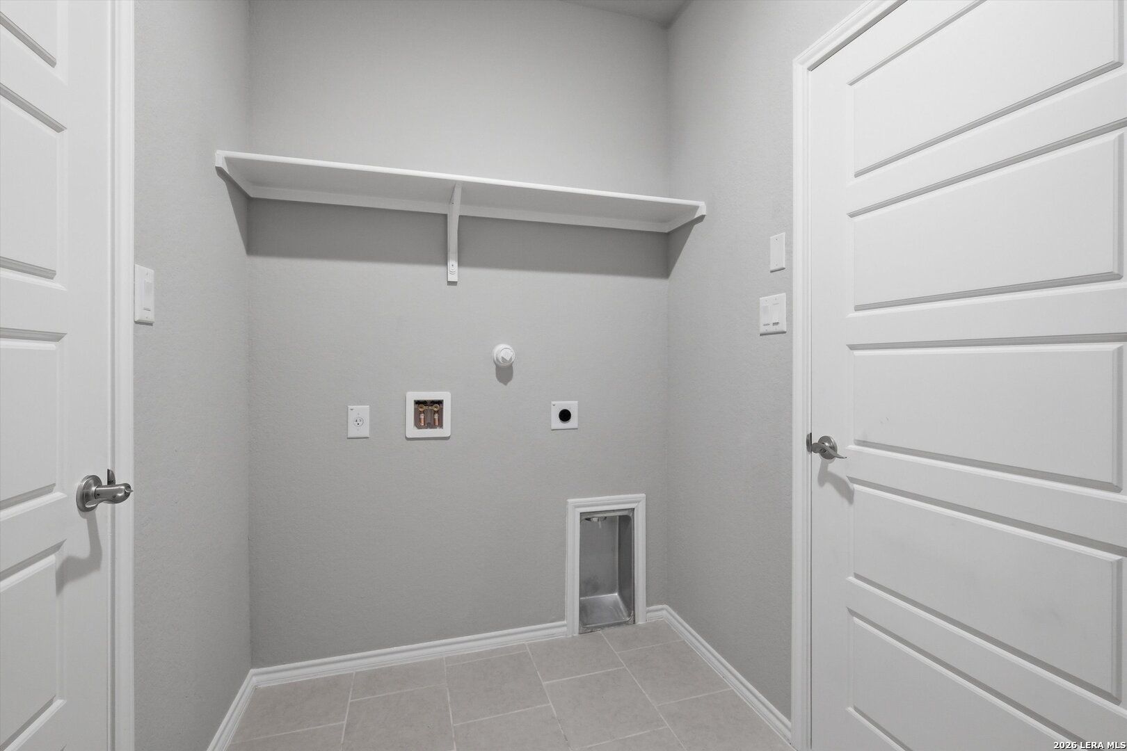 Modern laundry room with white floating shelf, washer-dryer hookups, and gray tile floor in Davidson Homes The Frio B, Agave San Antonio
