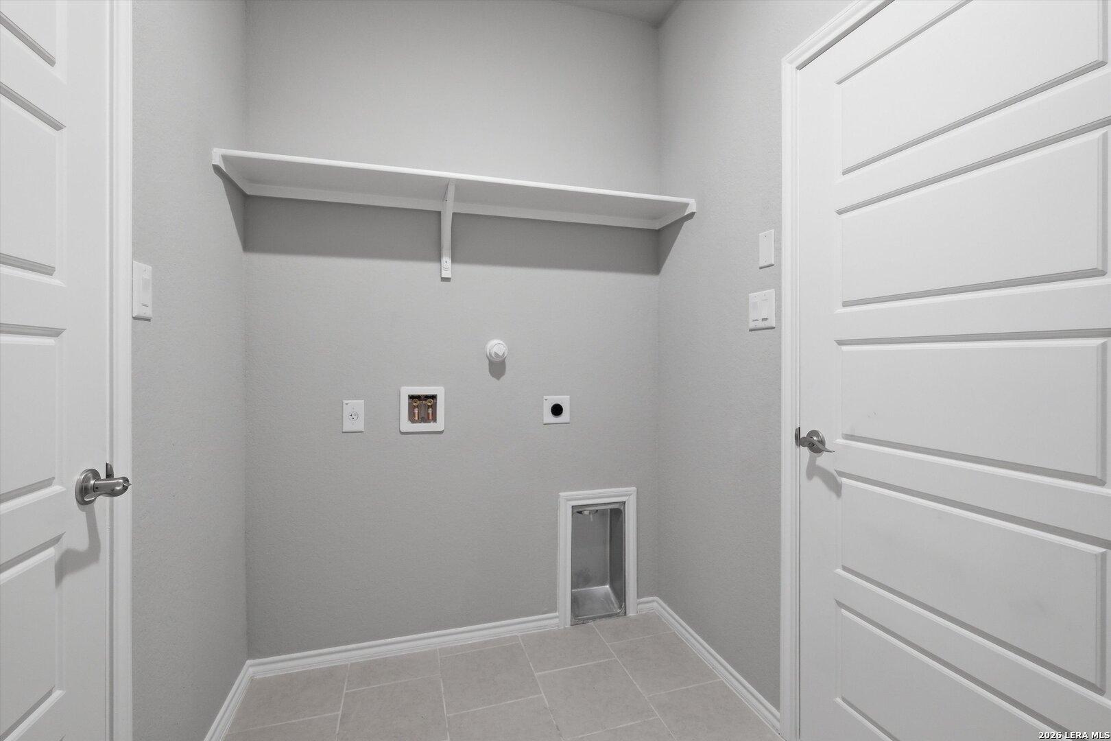 Modern laundry room with white floating shelf, washer-dryer hookups, and gray tile floor in Davidson Homes The Frio B, Agave San Antonio