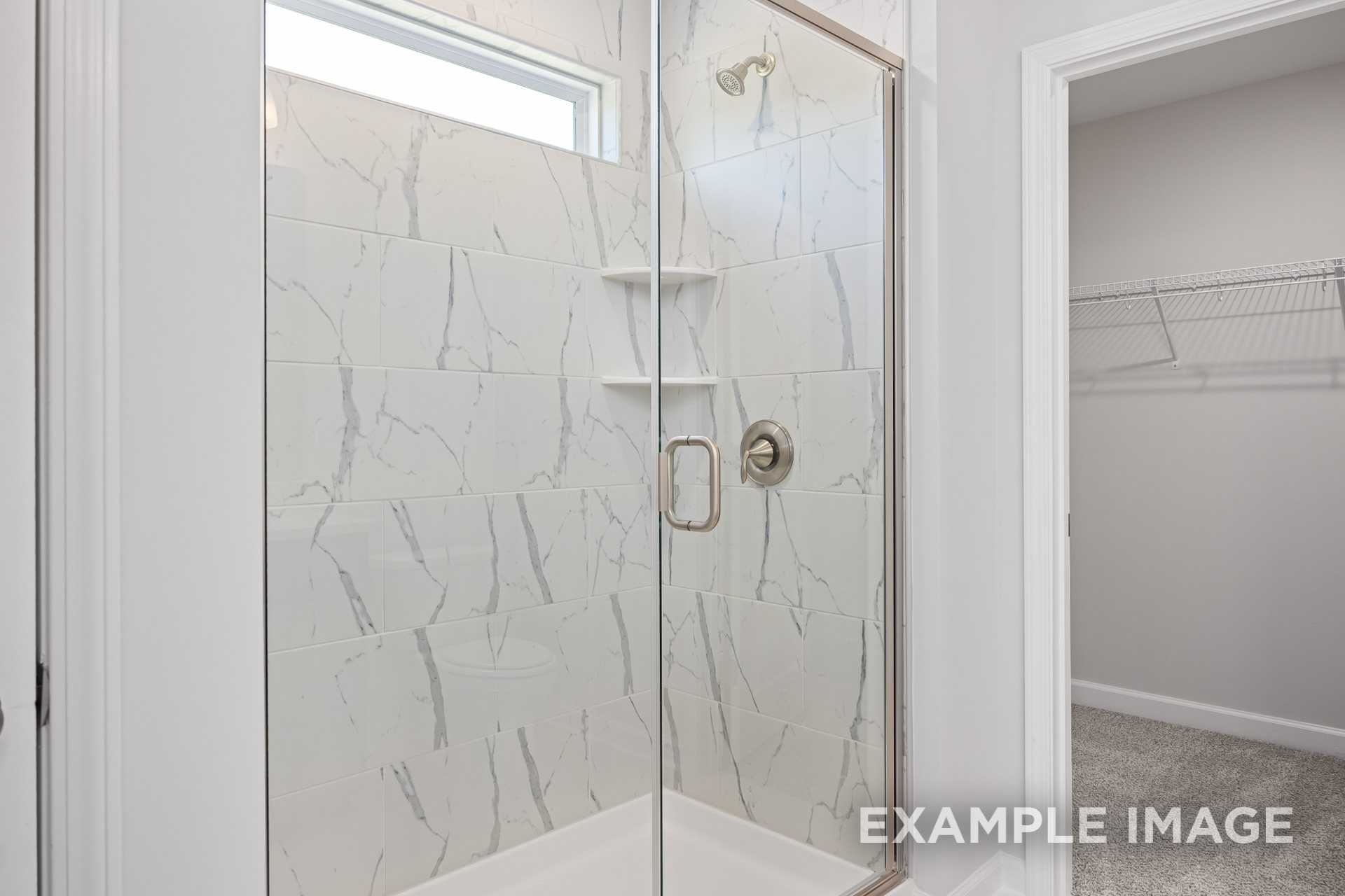 Spacious master bathroom in The Grace C featuring frameless glass walk-in shower with white veined tile and adjacent walk-in closet