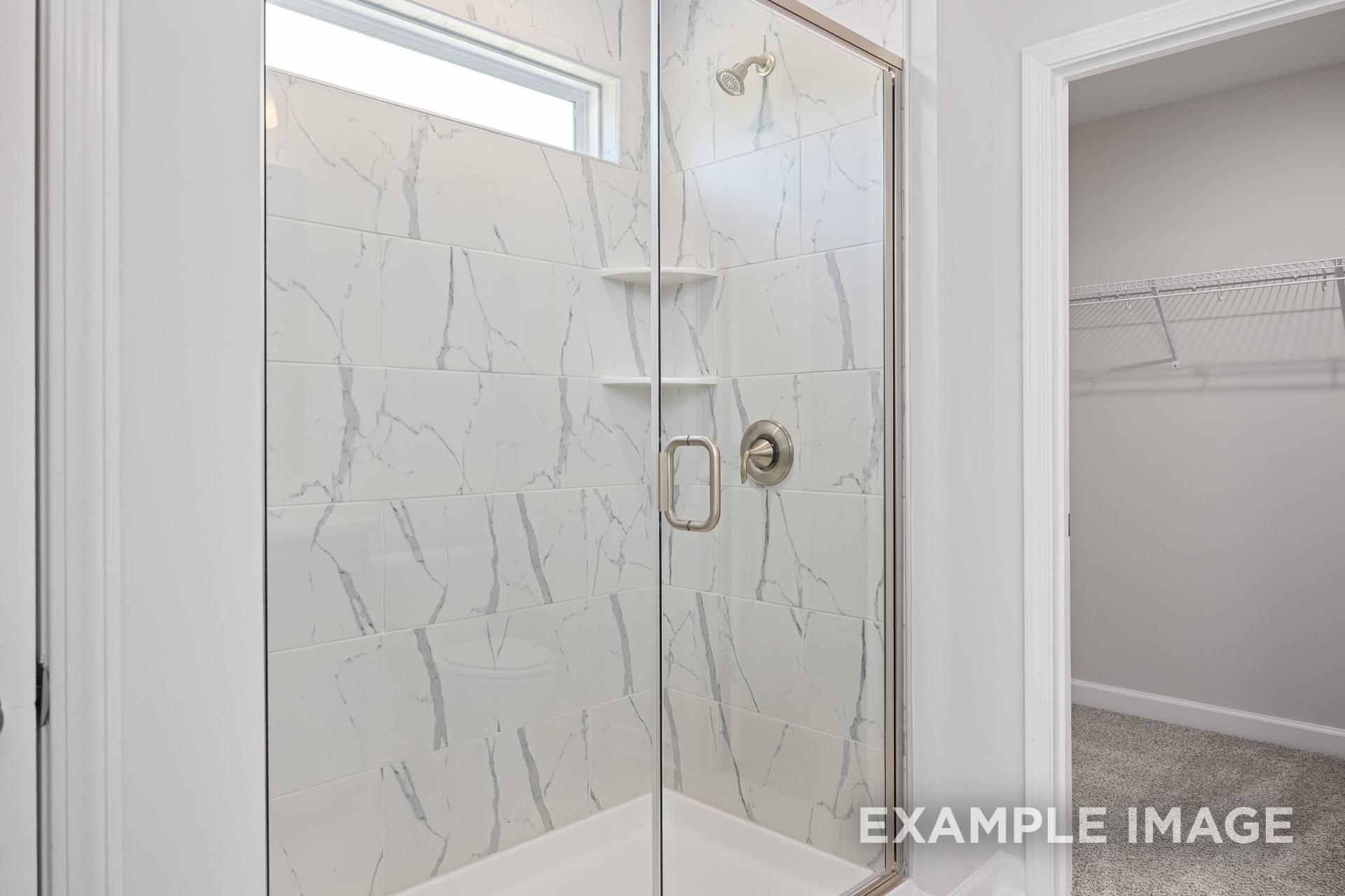 Spacious master bathroom in The Grace C featuring frameless glass walk-in shower with white veined tile and adjacent walk-in closet