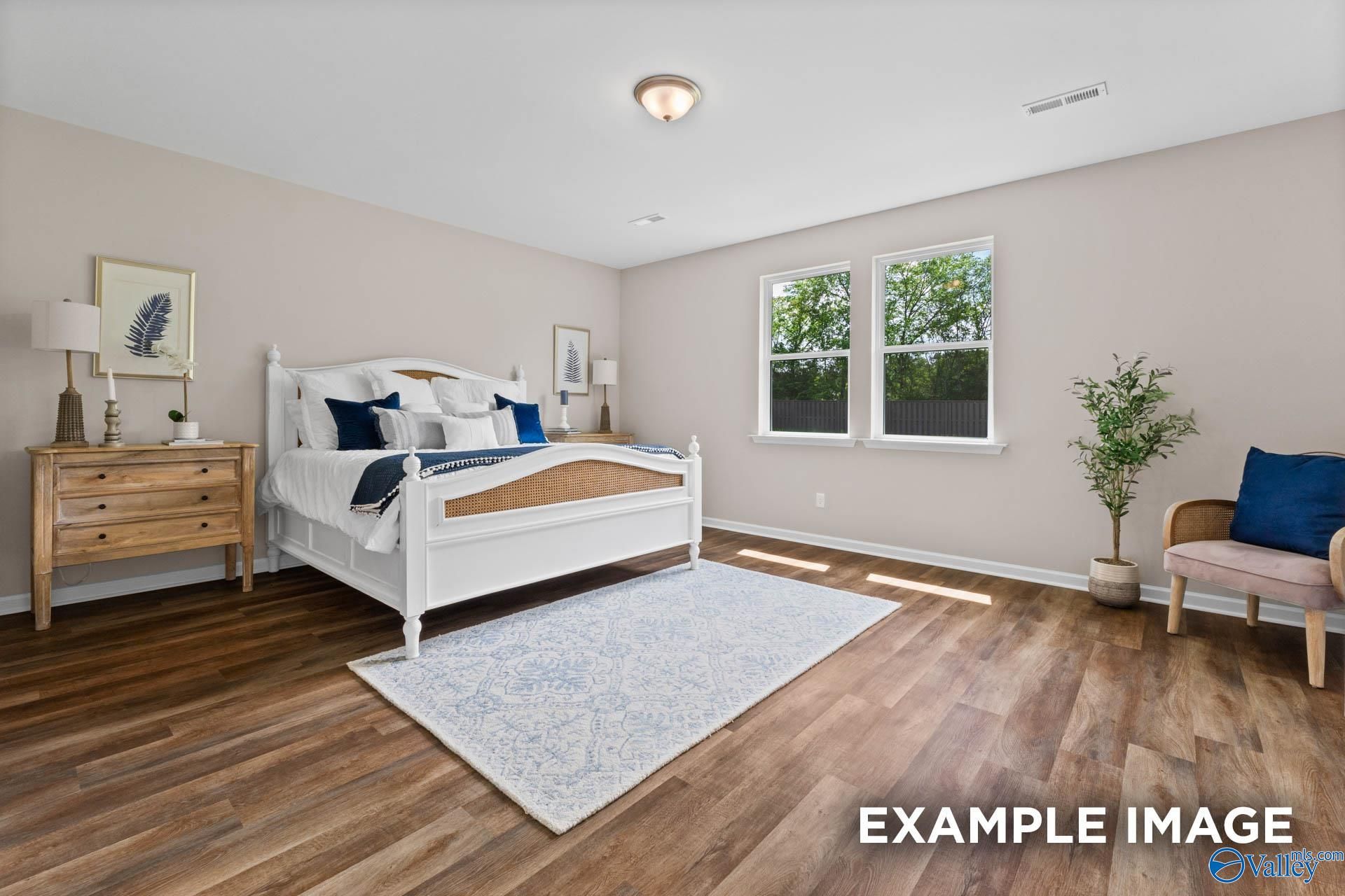 Cozy master bedroom with white wooden bed, blue accents, hardwood floors and large windows in Evermore Homes The Arcadia M, Owens Cross Roads, Alabama