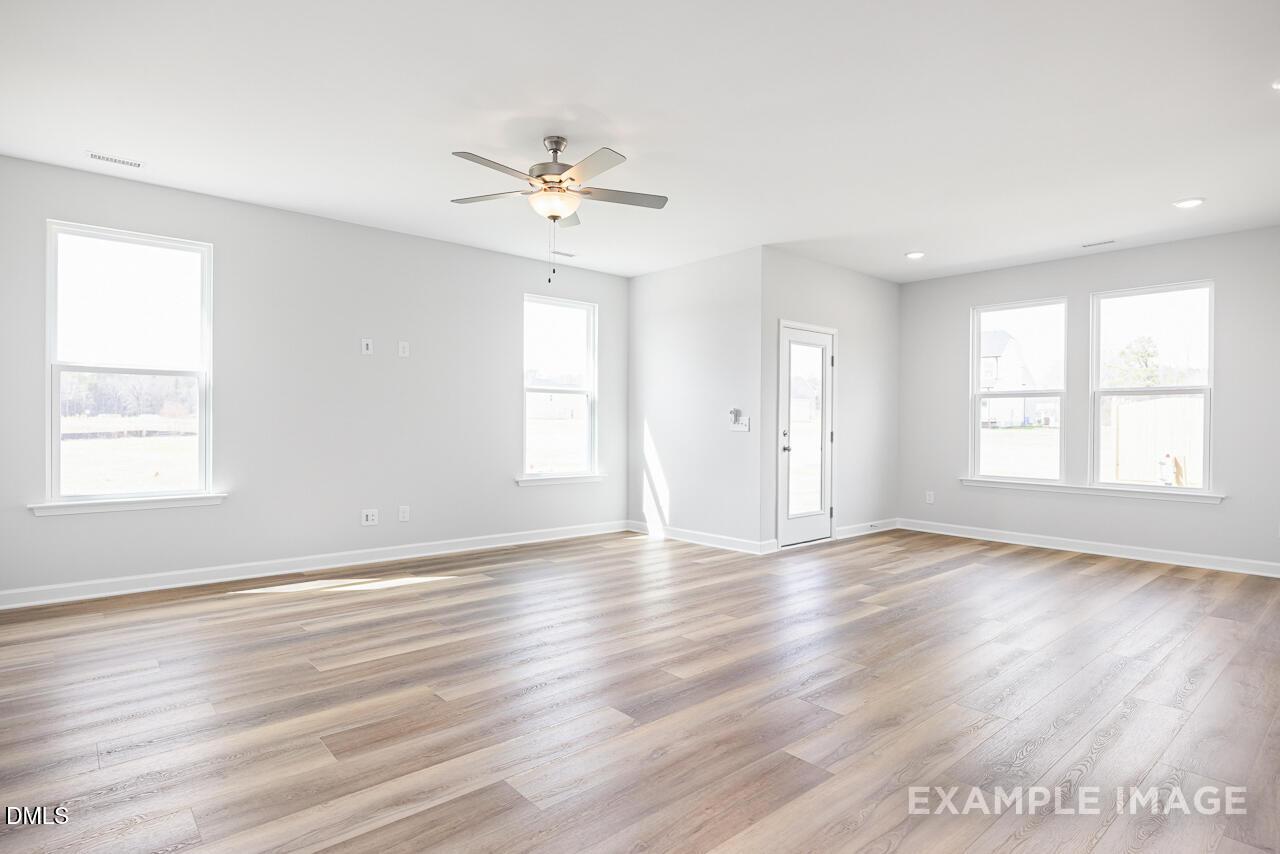 Spacious living room with light gray walls, large windows, ceiling fan, and hardwood floors in 4-bedroom Daphne C home, Zebulon, NC