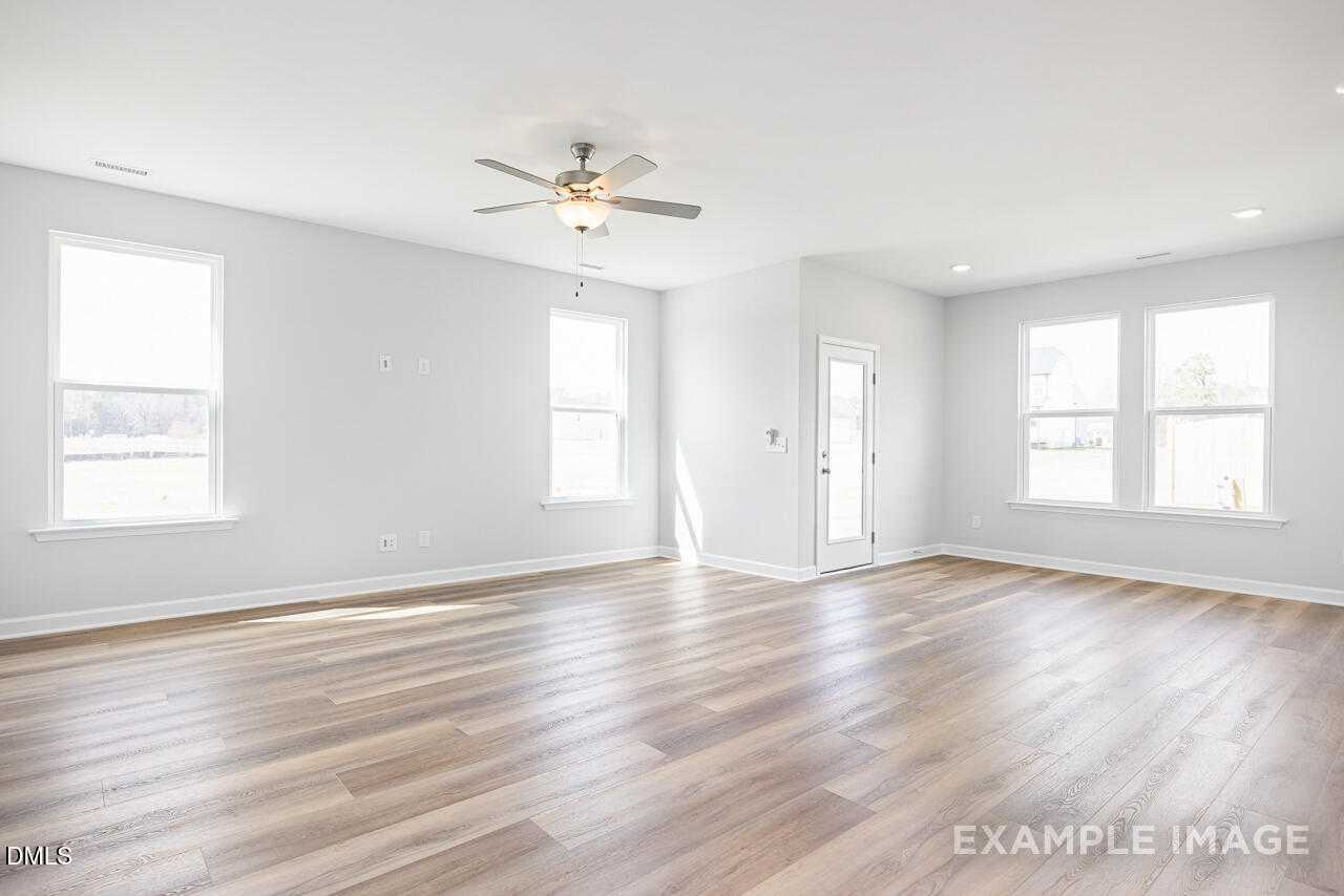 Spacious great room with hardwood floors, ceiling fan, large windows, and light gray walls in The Daphne C, Lillington, NC