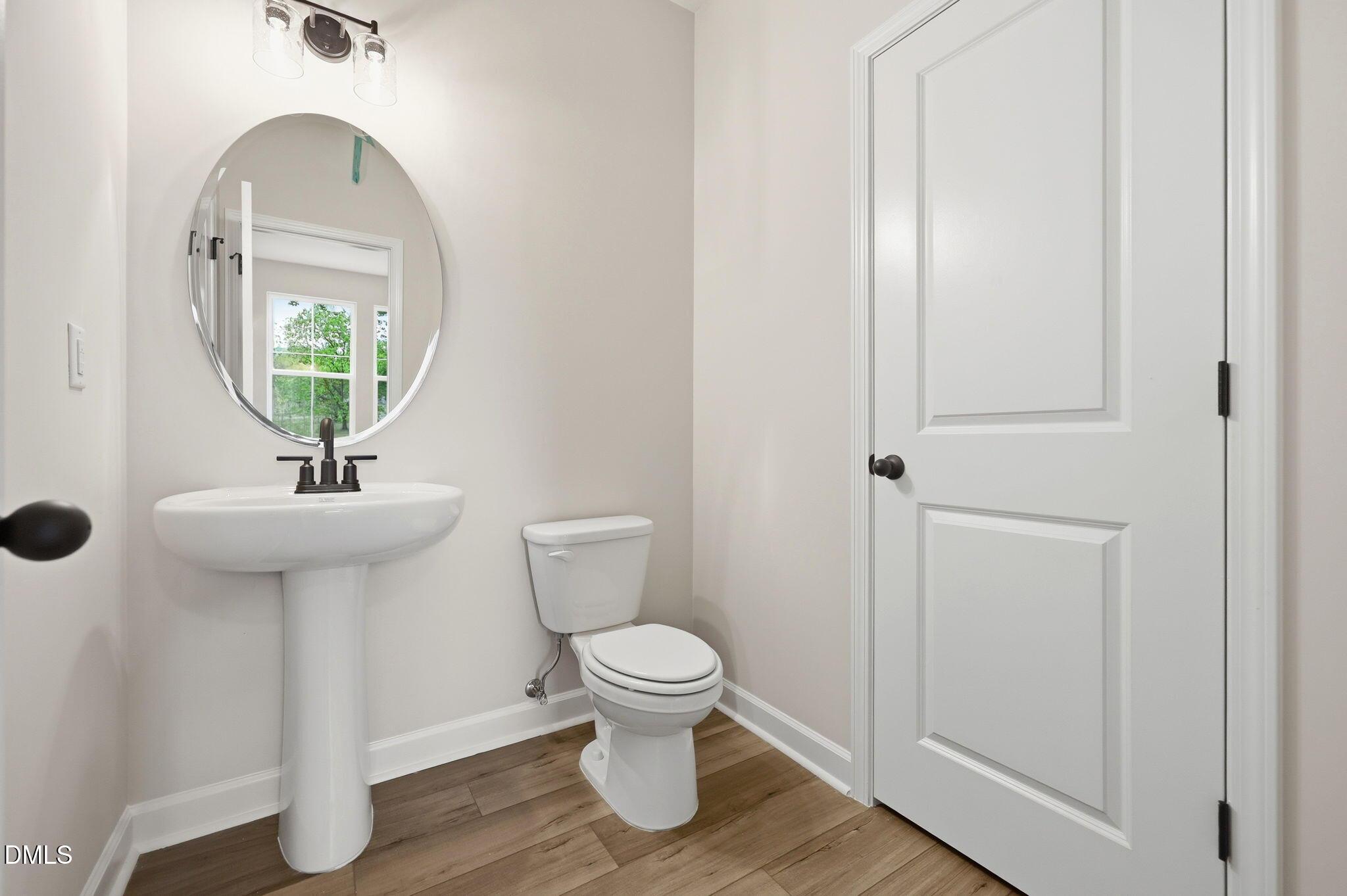 Modern half bath with pedestal sink, oval mirror, and wood-look flooring in The Mitchell floor plan at Camden Park, NC.
