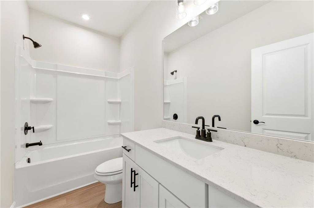 Modern white bathroom featuring subway tile shower, quartz vanity, tub, and black fixtures in The Daphne C, Loganville, GA