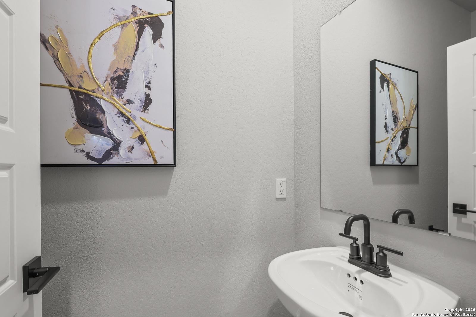 Modern powder room featuring abstract gold wall art, white vanity sink, black faucet, and large mirror in Davidson Homes The Murray K, San Antonio