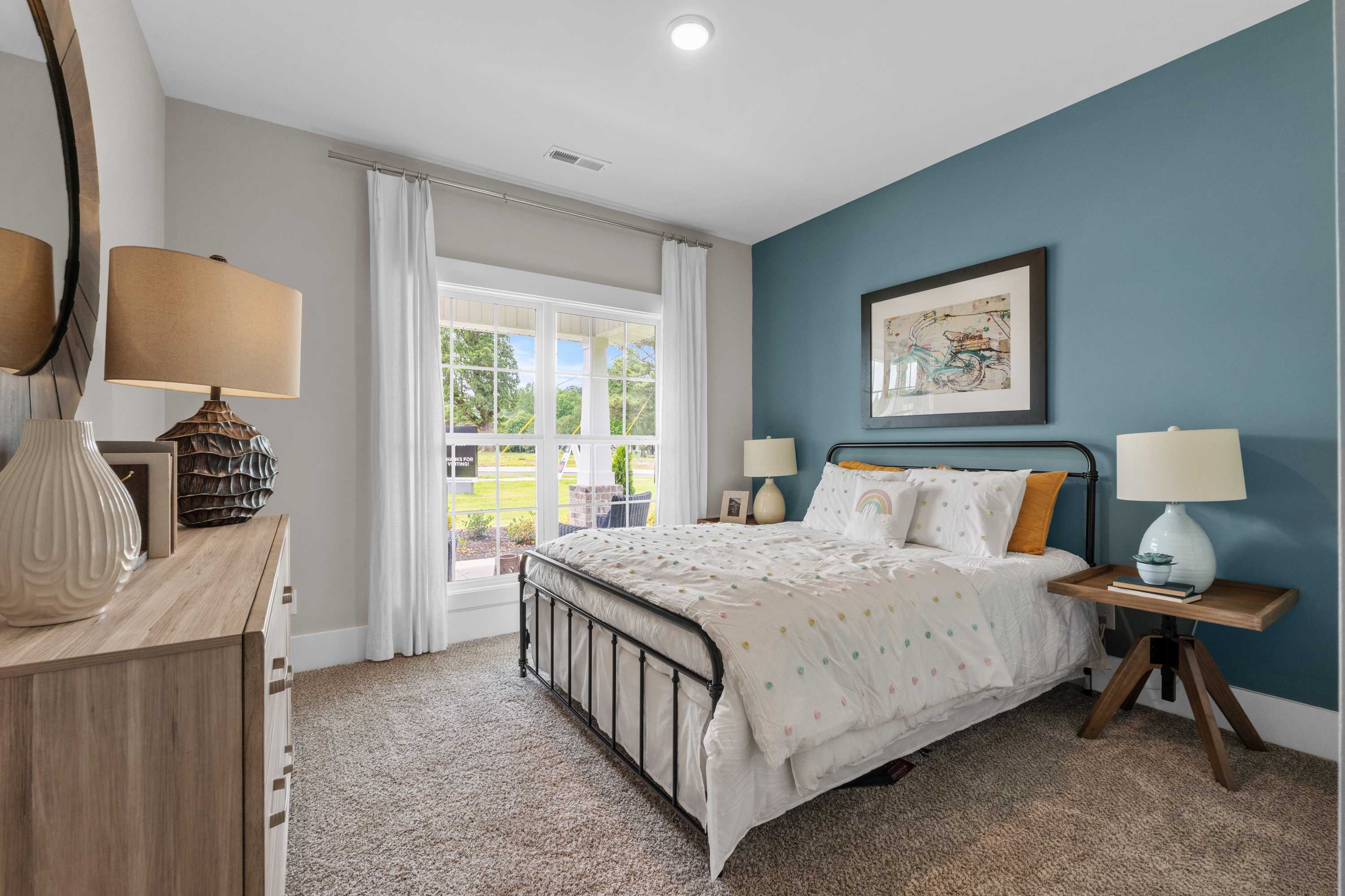 Cozy bedroom interior at The Highlands in Arab Alabama with teal walls, white iron bed, patterned duvet, and garden-view window