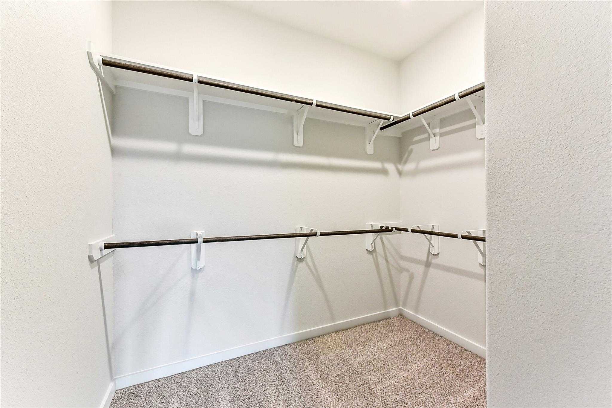 Spacious walk-in closet with wooden shelves and hanging rods in Davidson Homes The Laguna C, Sierra Vista, Rosharon, Texas
