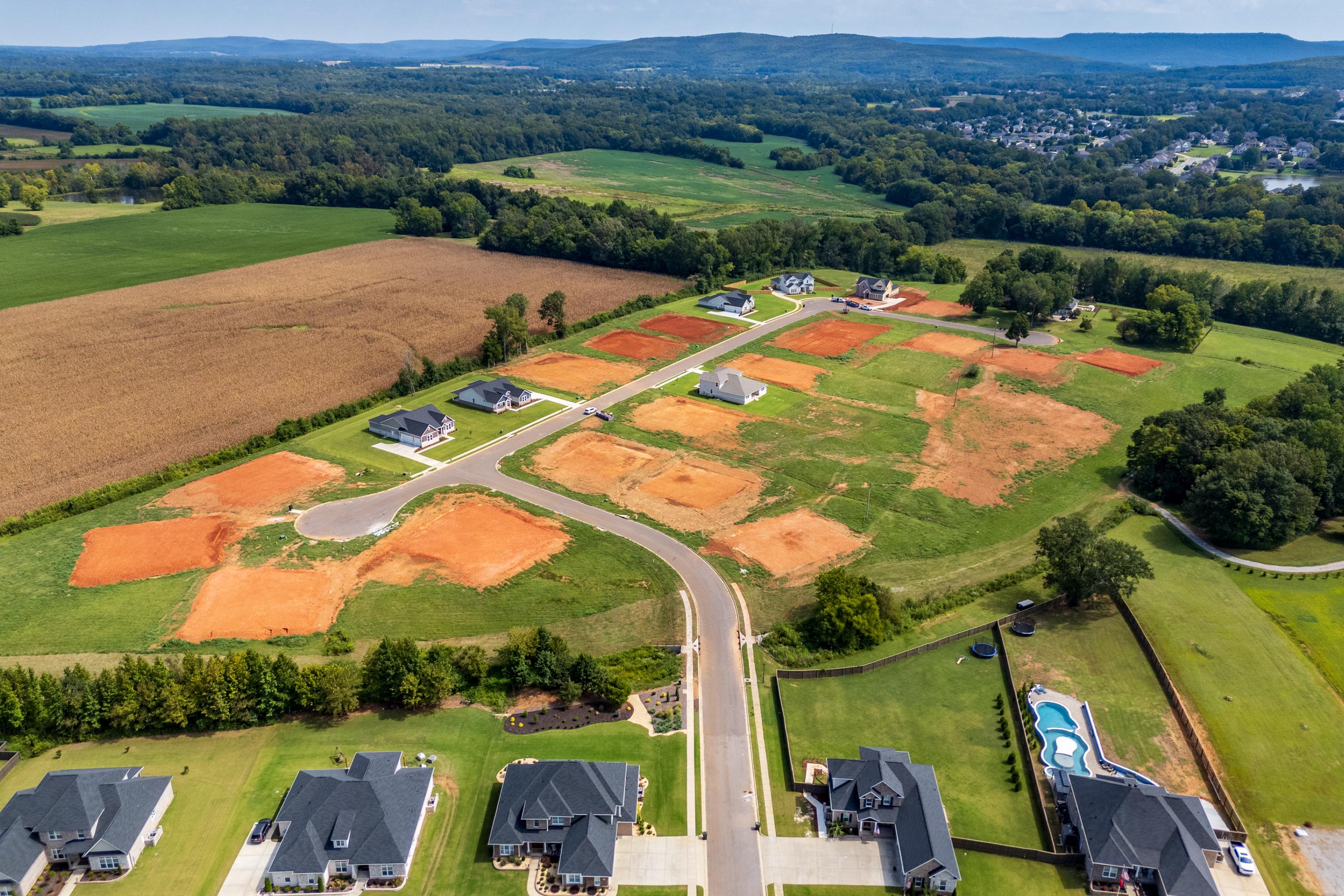 Aerial view of Riverton Preserve new homes in Huntsville Alabama with construction sites, dark-roofed houses, red clay lots and surrounding fields