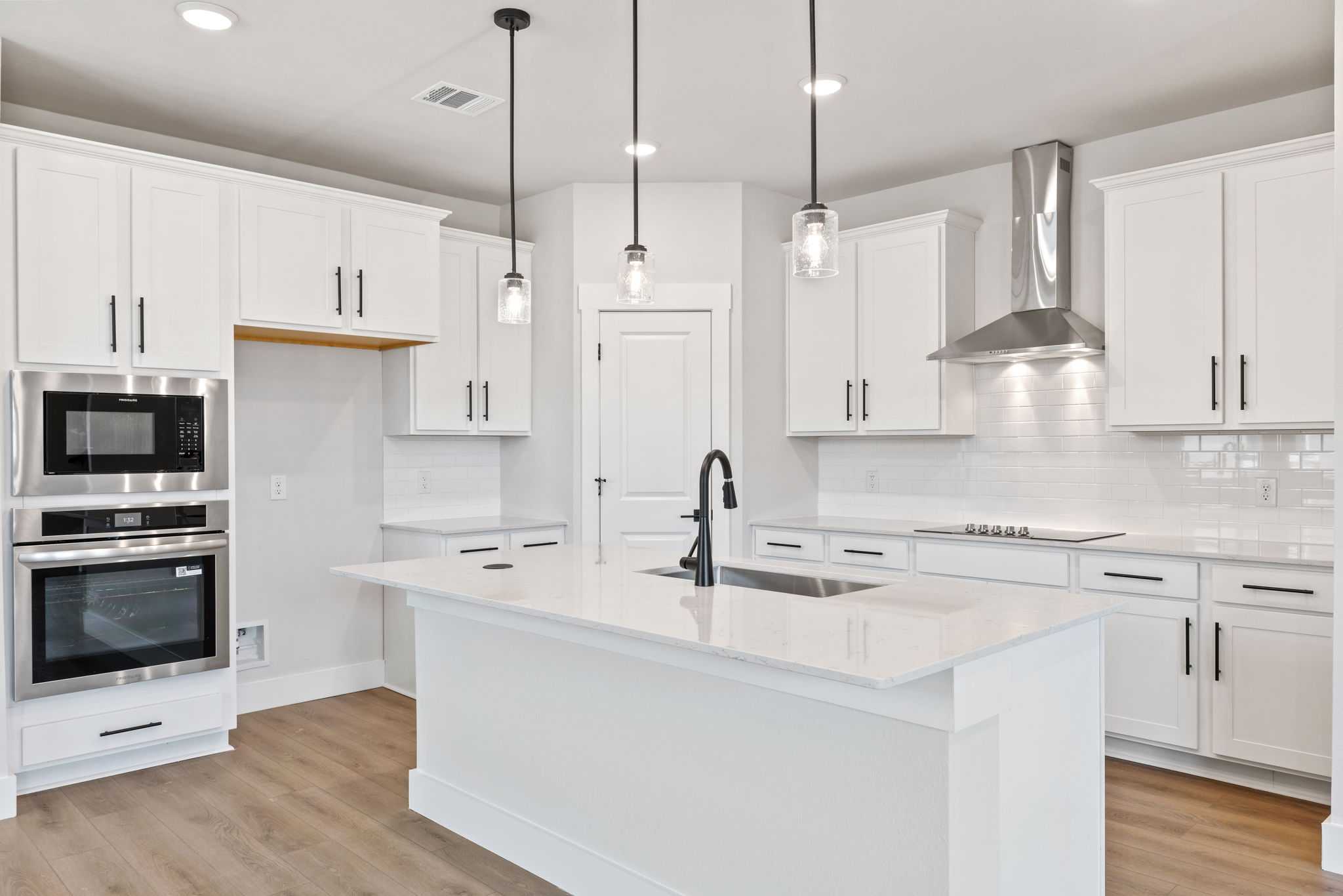 Bright white kitchen with large island sink, double oven, stainless hood in Davidson Homes The Durham C, Wylie, Texas