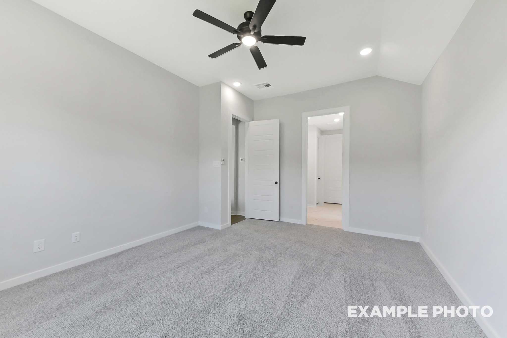Spacious master bedroom in The Sequoia home with light gray walls, plush gray carpet, black ceiling fan, and open doorways