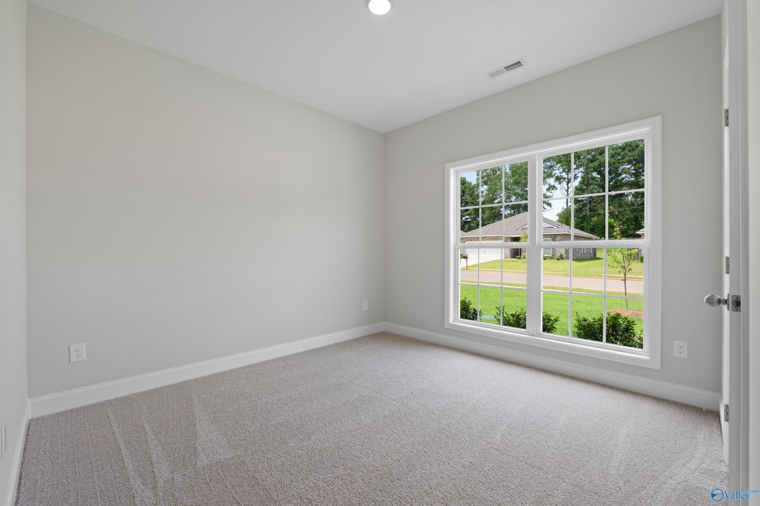 Bright secondary bedroom with gray walls, carpeted floor, and large window view of green lawn in Davidson Homes The Franklin C, Harvest, Alabama