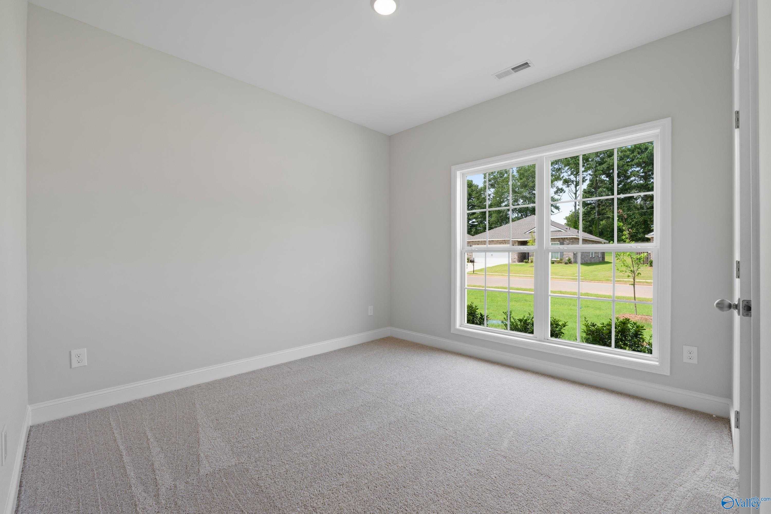 Bright secondary bedroom with gray walls, carpeted floor, and large window view of green lawn in Davidson Homes The Franklin C, Harvest, Alabama