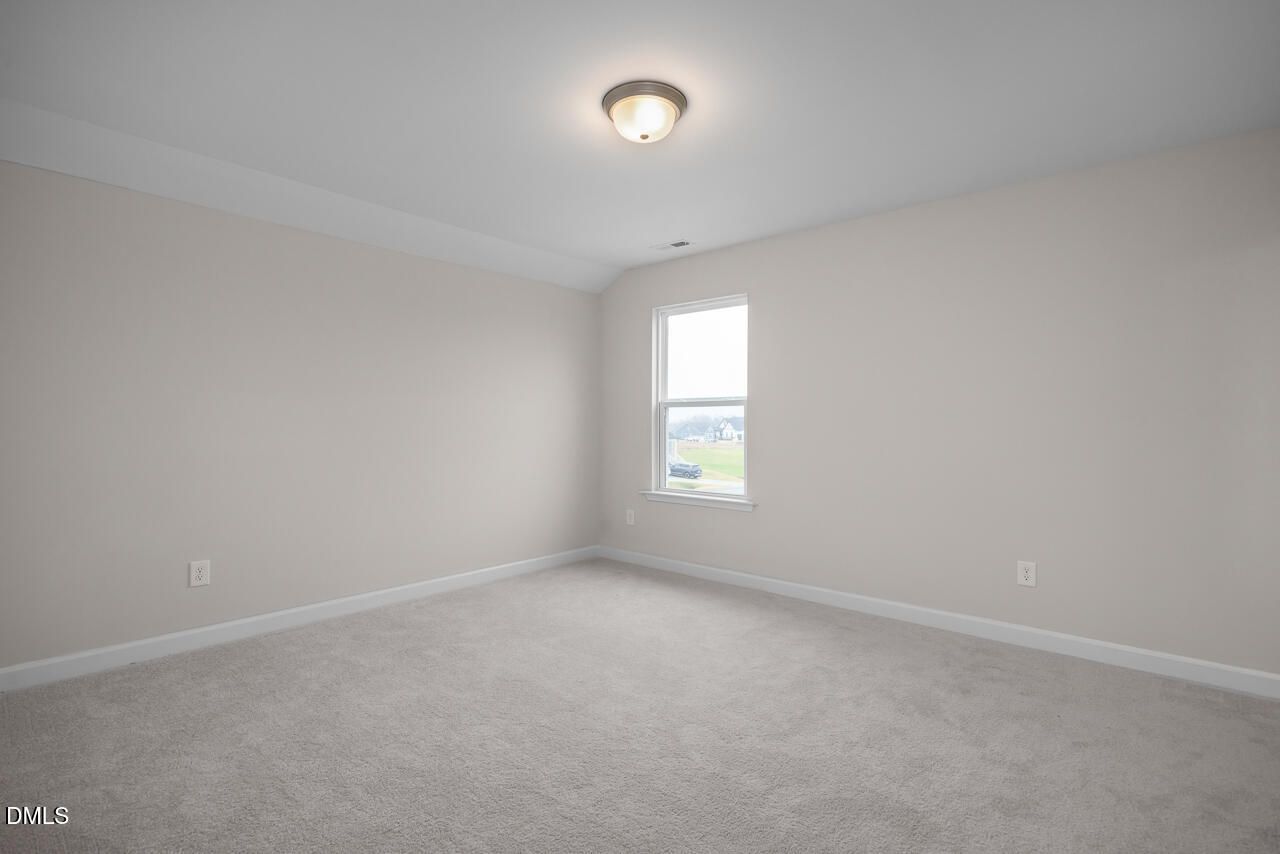 Empty bedroom with light gray walls, neutral carpet, large window, ceiling light in Davidson Homes The Cypress D II, Angier, NC