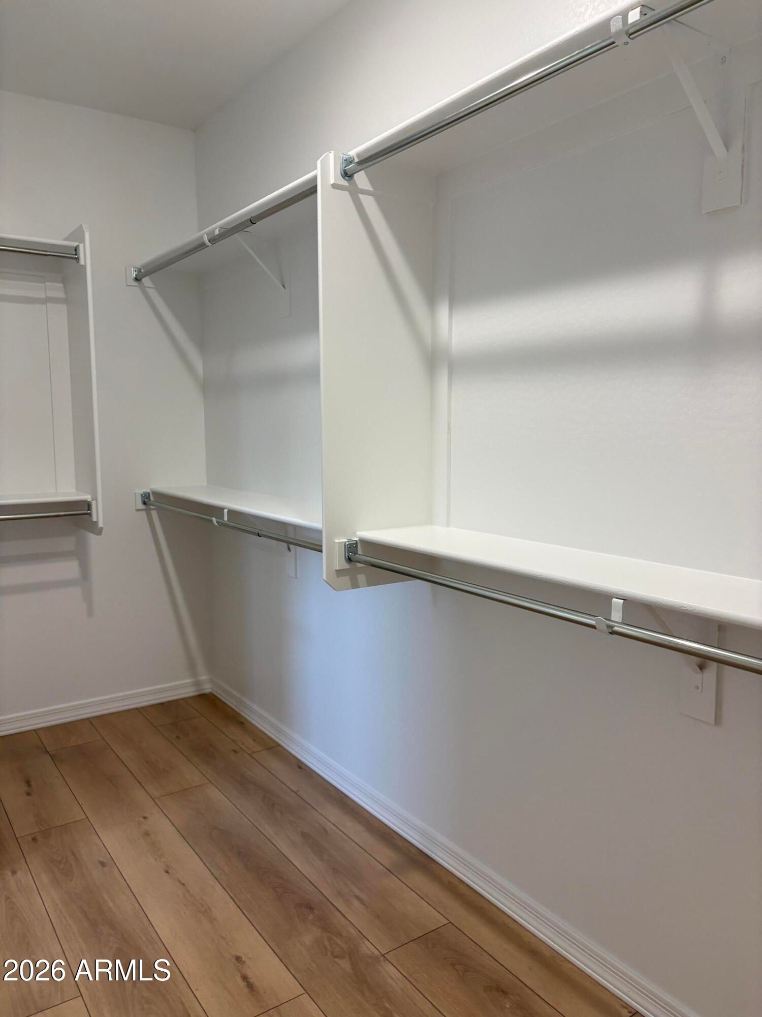 Walk-in closet with white shelving, hanging rods, and wood-look flooring in Davidson Homes The Evergreen B, Cottonwood, Arizona