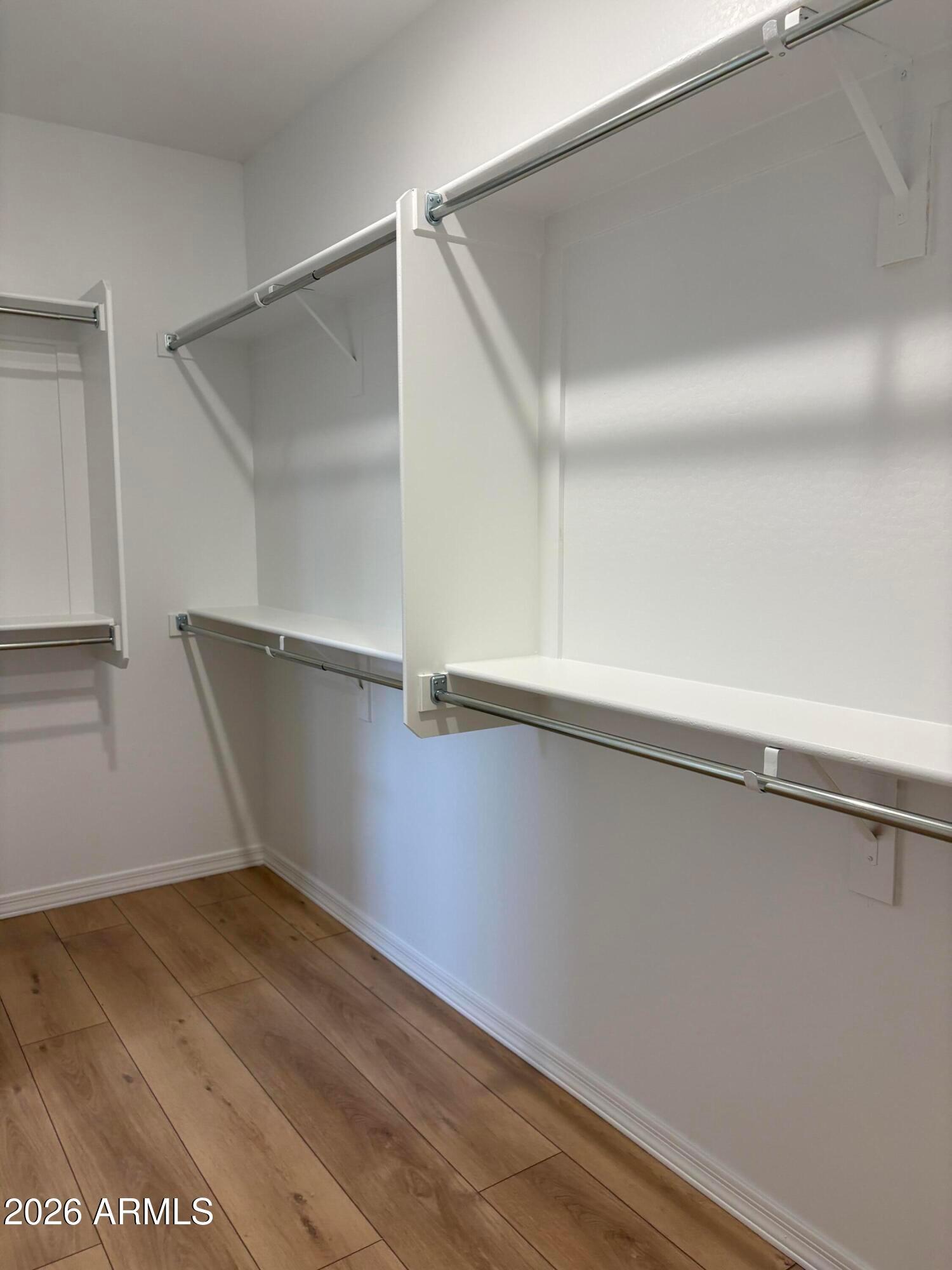 Walk-in closet with white shelving, hanging rods, and wood-look flooring in Davidson Homes The Evergreen B, Cottonwood, Arizona