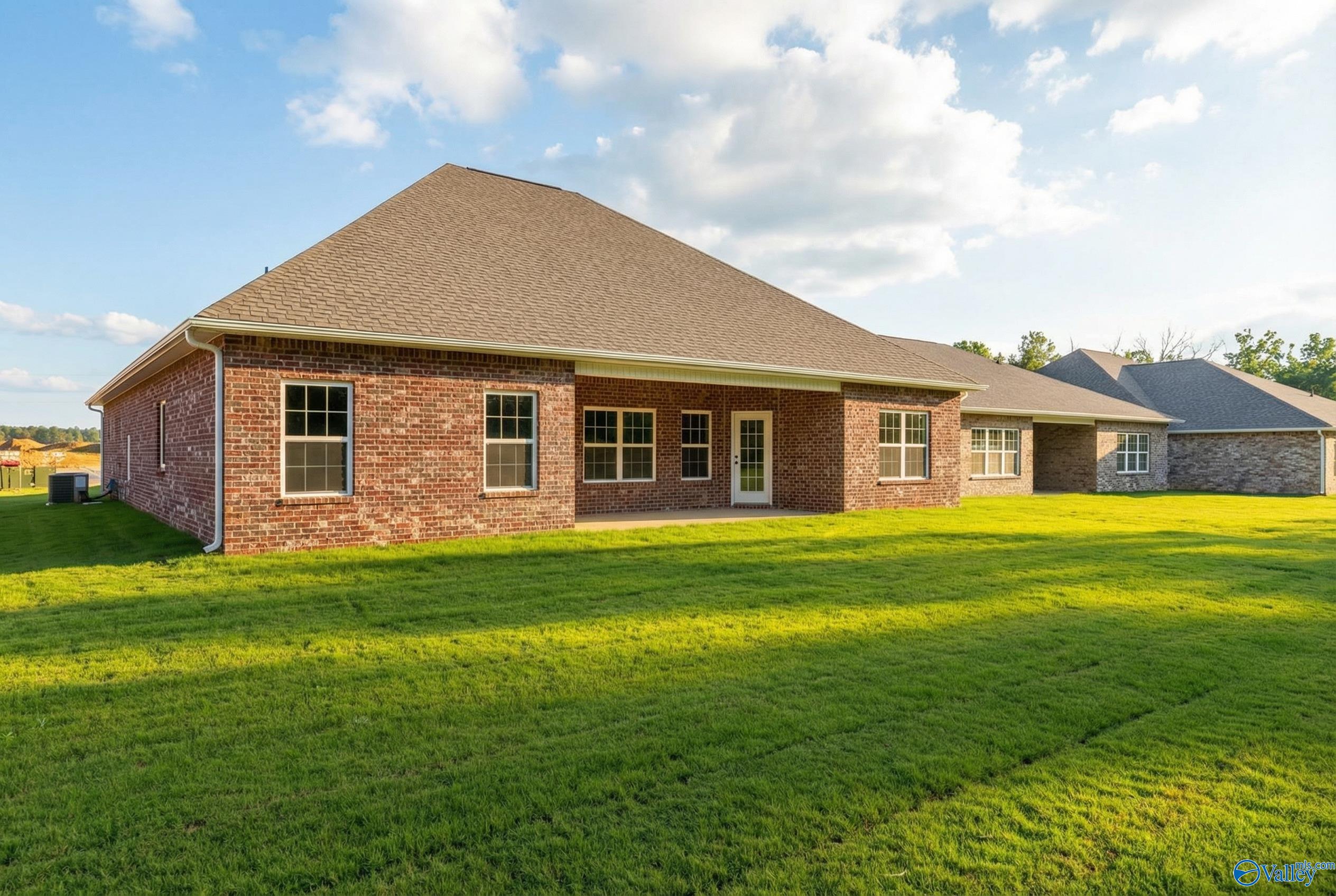 Brick single-story home rear with covered patio, large windows, gabled roof, lush green lawn in Cain Park, Hartselle, Alabama - Rockford B by Davidson Homes