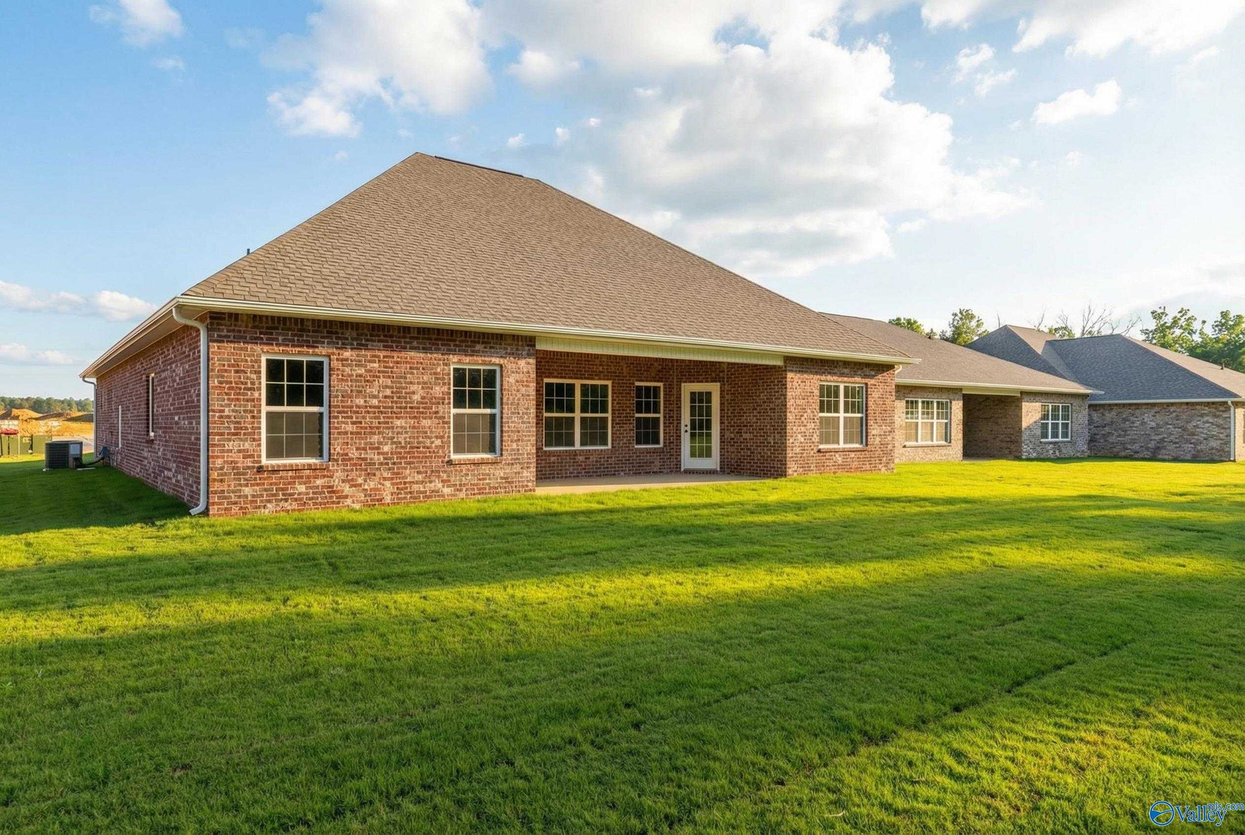 Brick single-story home rear with covered patio, large windows, gabled roof, lush green lawn in Cain Park, Hartselle, Alabama - Rockford B by Davidson Homes