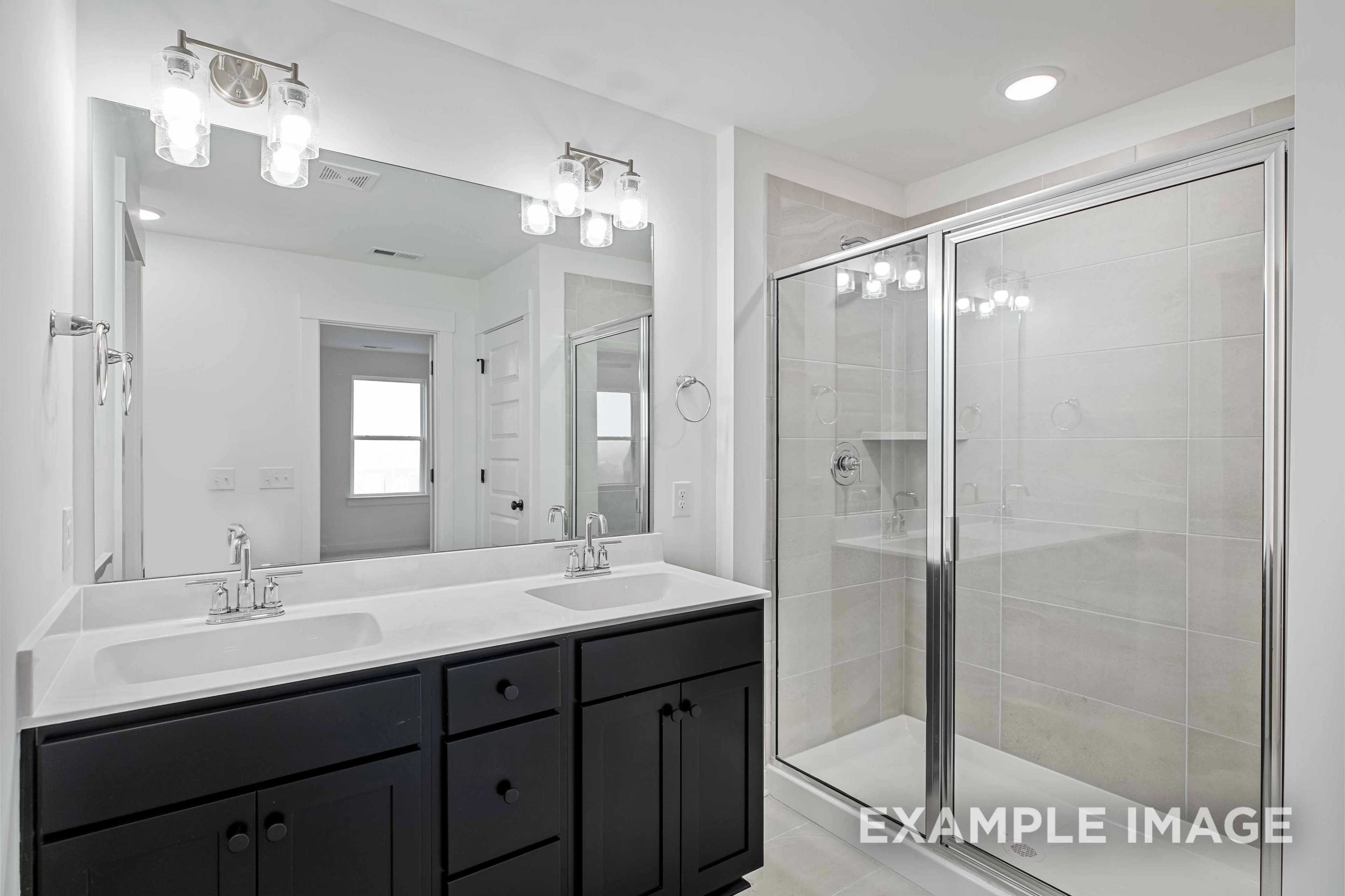 Modern master bathroom in The Charleston with double black vanity, large mirror, and frameless glass shower