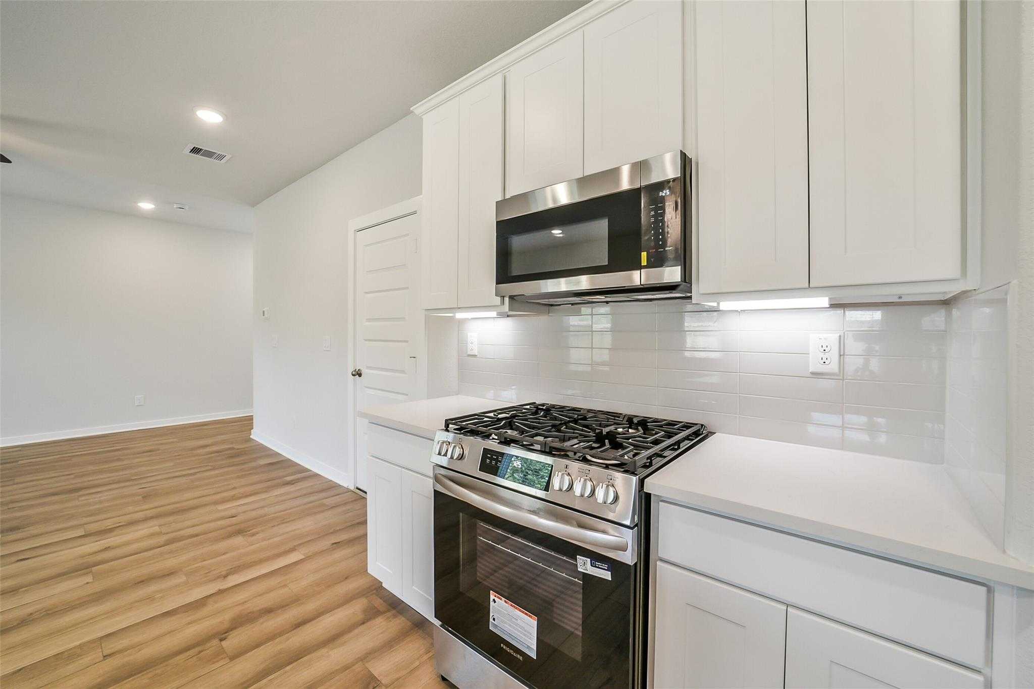 Modern white kitchen with stainless steel gas range, oven, microwave, quartz counters, and subway tile in Davidson Homes The Trinity F, Magnolia, Texas