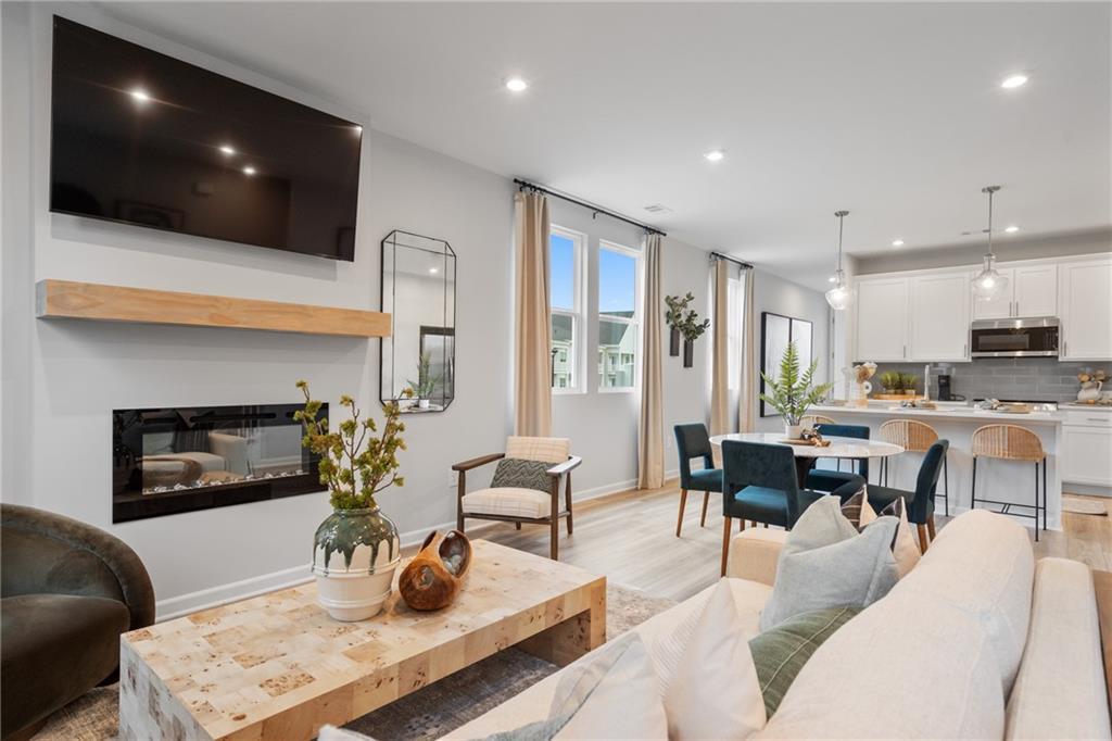 Cozy open living room with gas fireplace, mounted TV, beige sofa, and adjacent dining area in Davidson Homes The Wilmington B, Emerson, Georgia