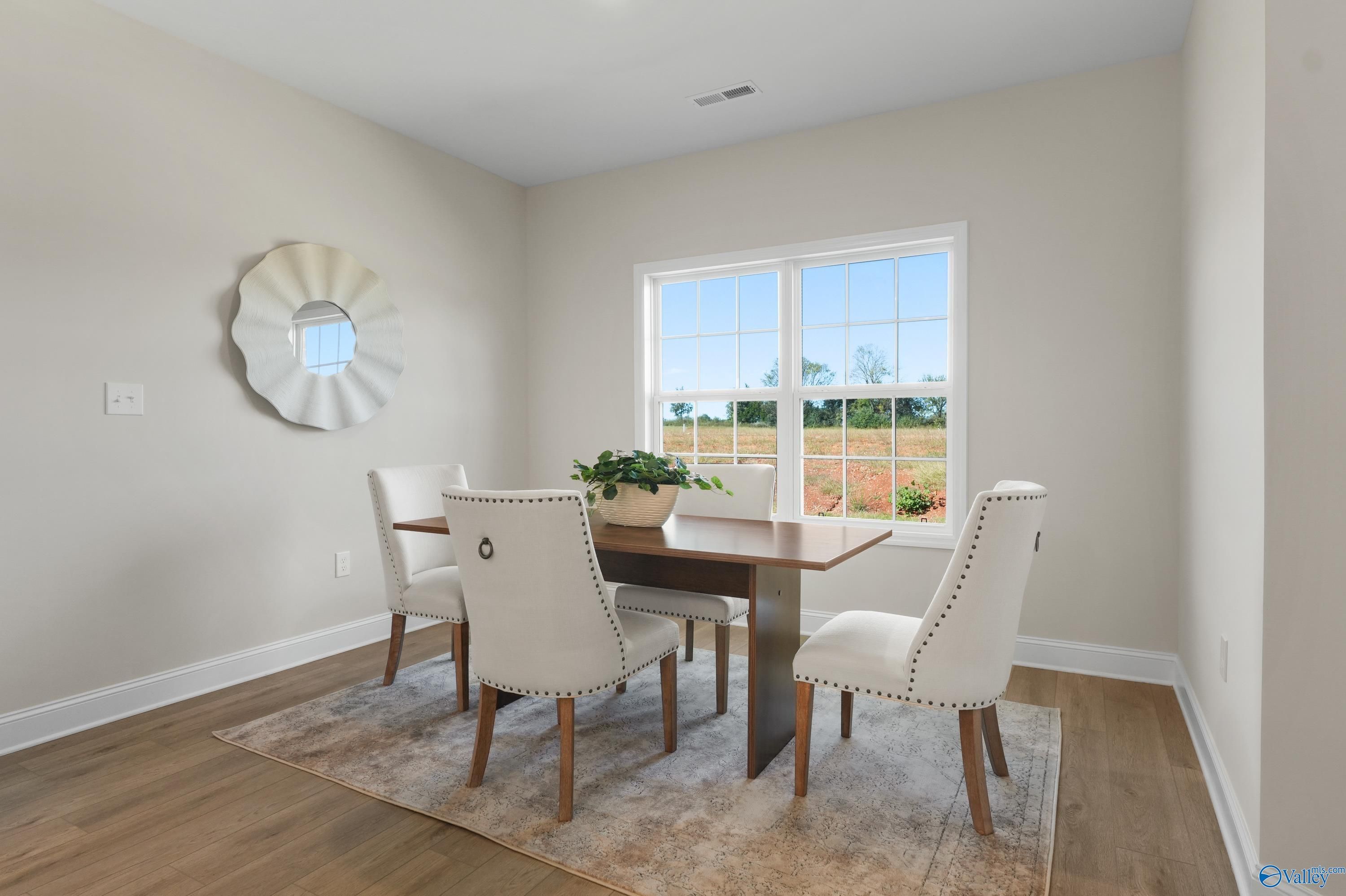 Elegant dining room featuring wooden table, tufted chairs, round mirror, and garden view window in Davidson Homes The Rockford B, Toney, Alabama