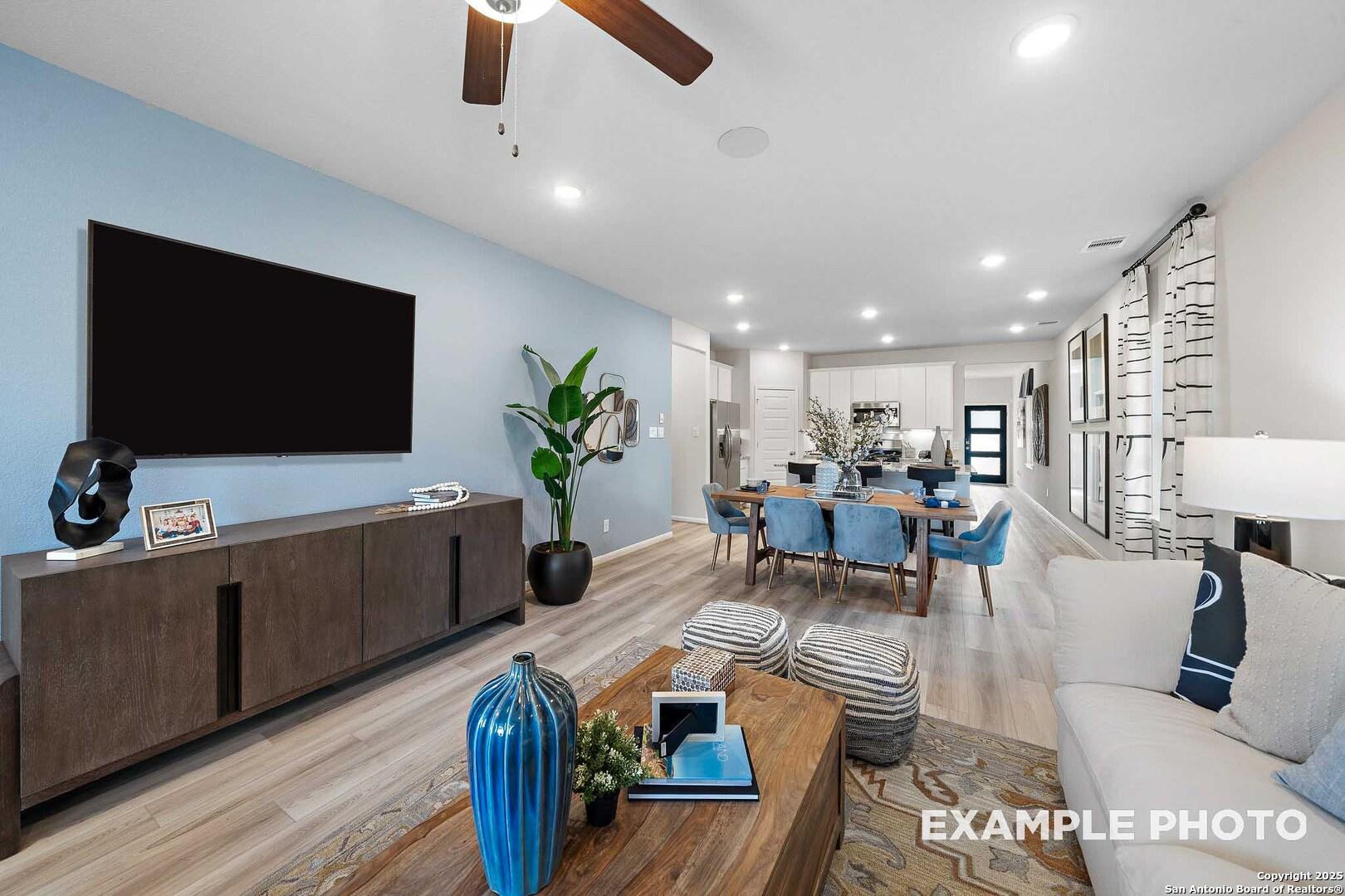 Modern open-concept living and dining area with mounted TV, ceiling fan, and wood floors in The San Marcos D by Davidson Homes, San Antonio