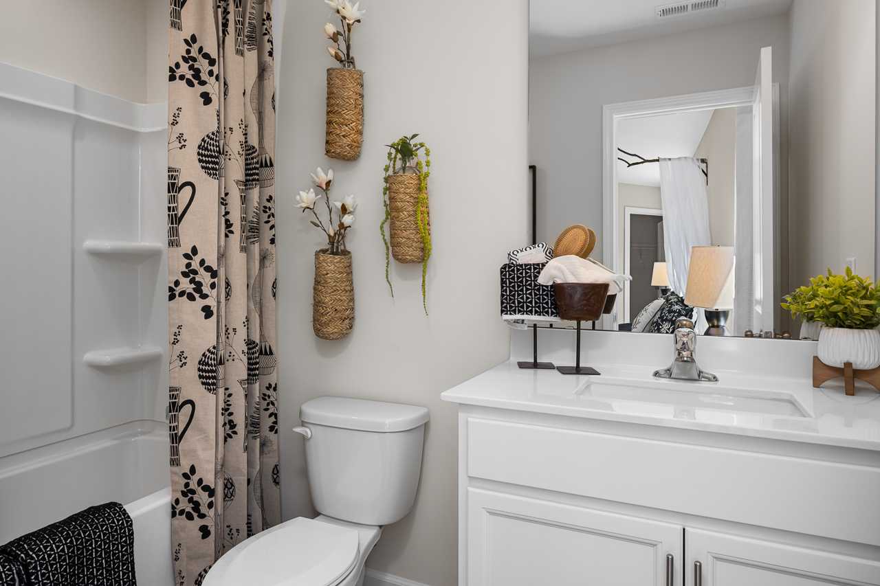 Modern bathroom at Wellers Knoll in Lillington NC featuring white vanity, glass shower with patterned curtain, woven plant baskets