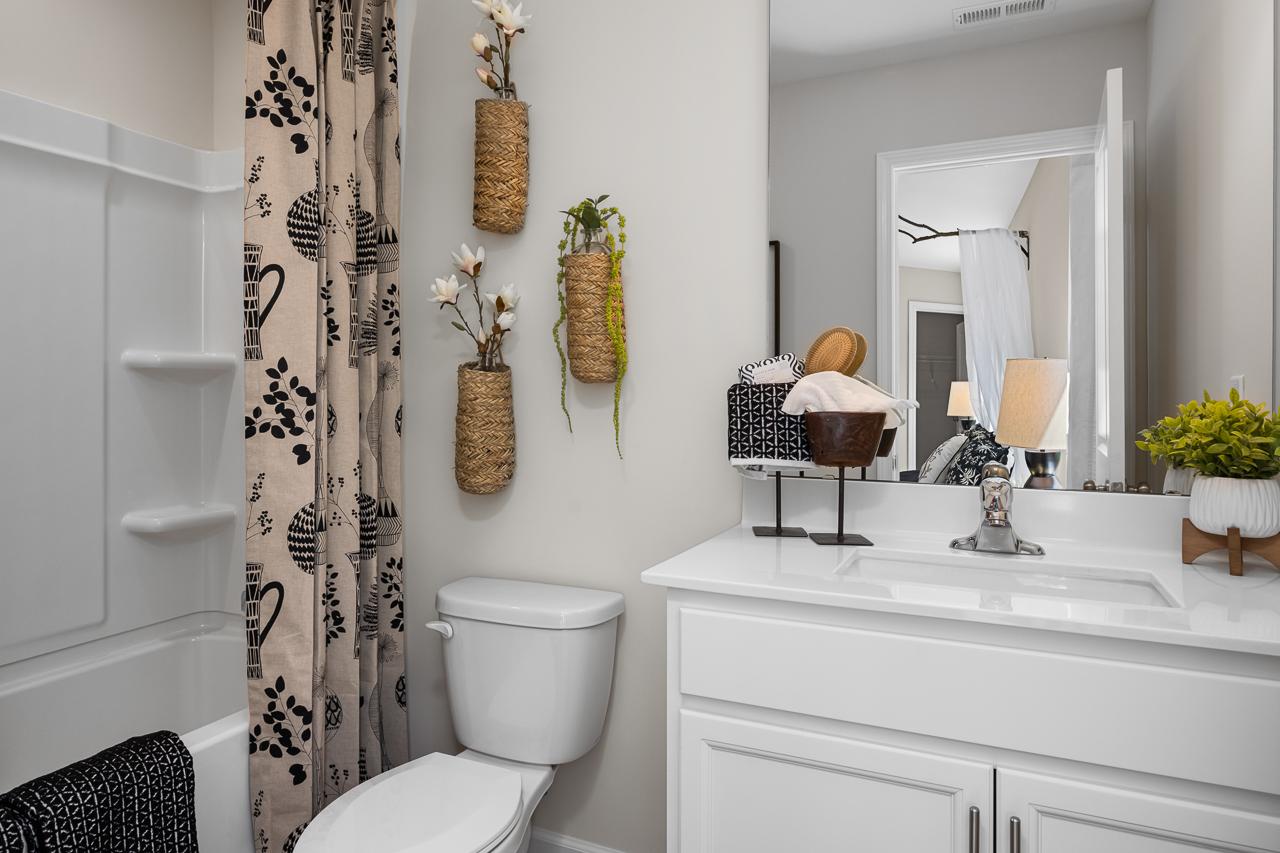 Modern bathroom at Wellers Knoll in Lillington NC featuring white vanity, glass shower with patterned curtain, woven plant baskets