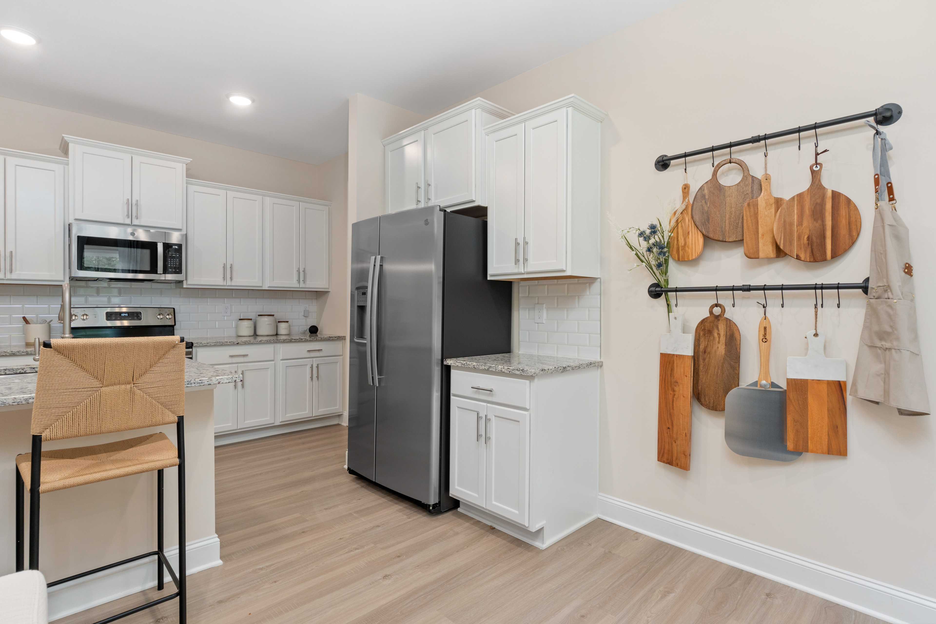 Spacious modern kitchen in Pavilion Huntsville AL with white cabinets, stainless steel fridge, subway tile backsplash, and hanging wooden utensils