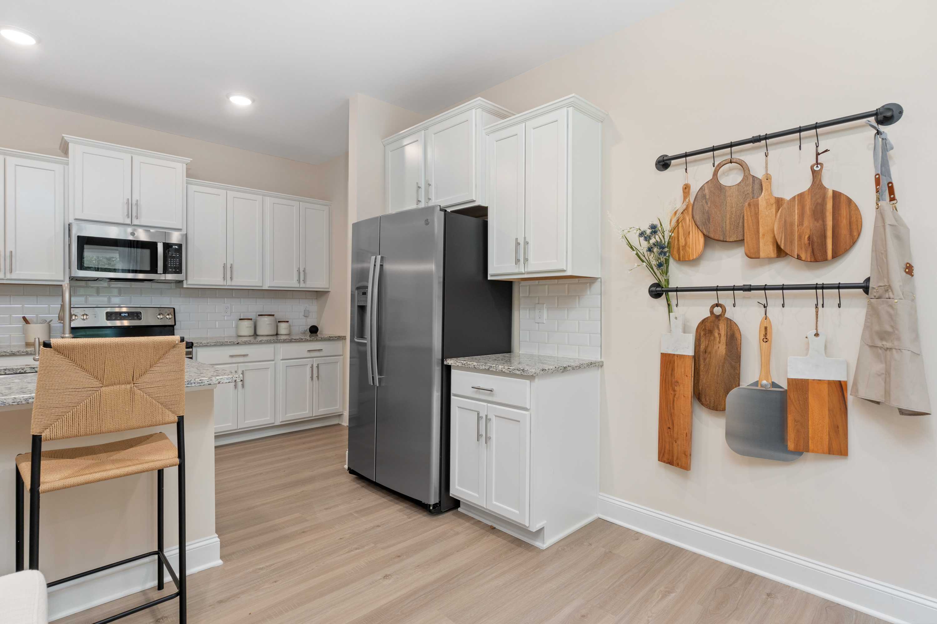 Spacious modern kitchen in Pavilion Huntsville AL with white cabinets, stainless steel fridge, subway tile backsplash, and hanging wooden utensils