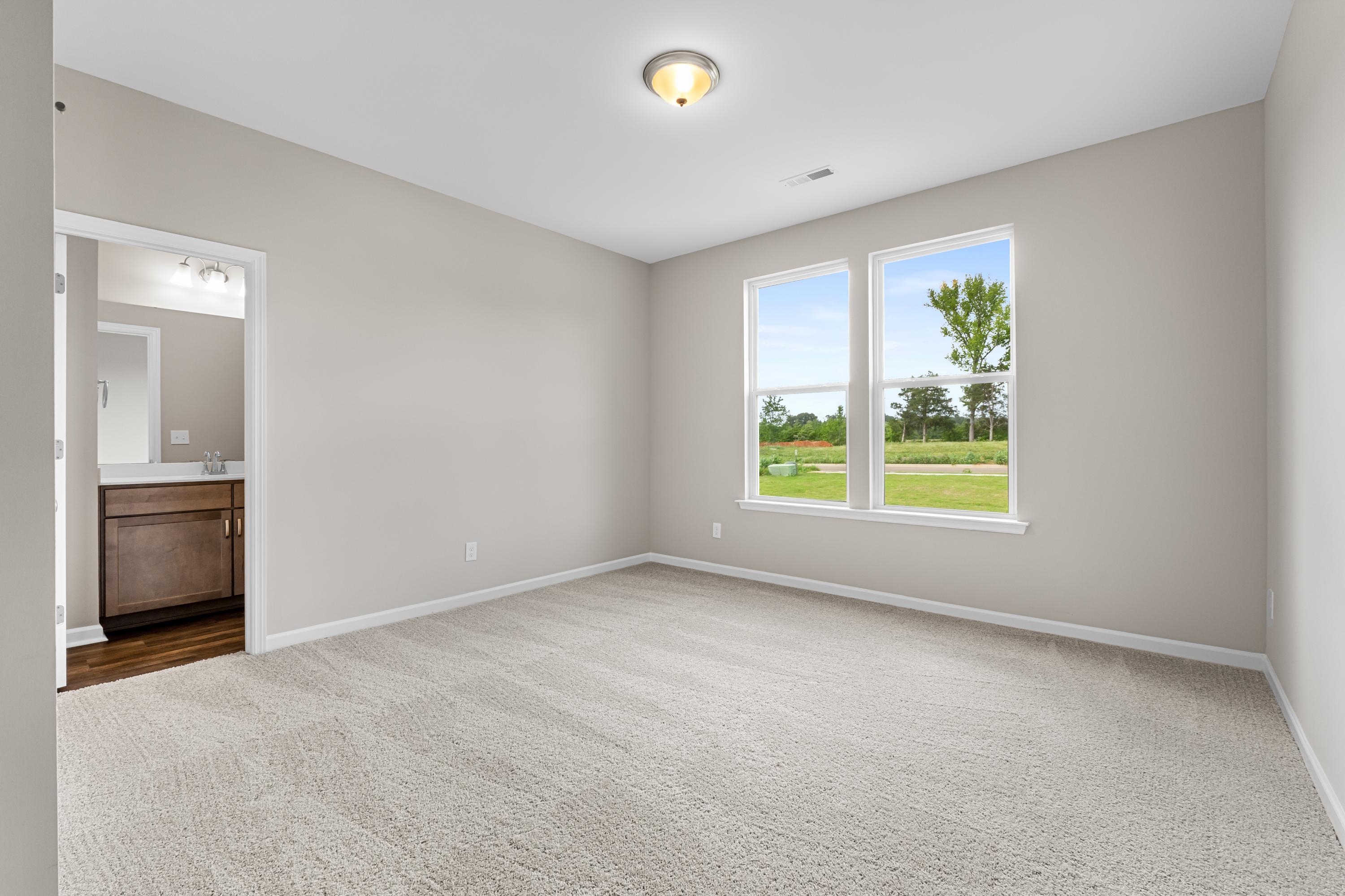 Spacious master bedroom in The Haven E featuring beige walls, carpeted floor, en-suite bath, and large windows with green yard view