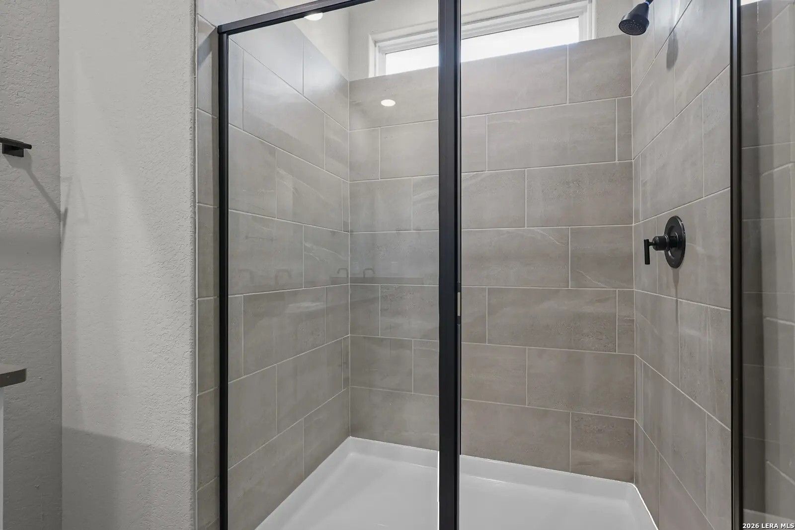 Modern walk-in shower with neutral tile and black fixtures in a Davidson Homes Glenwood E floor plan, San Antonio, TX.