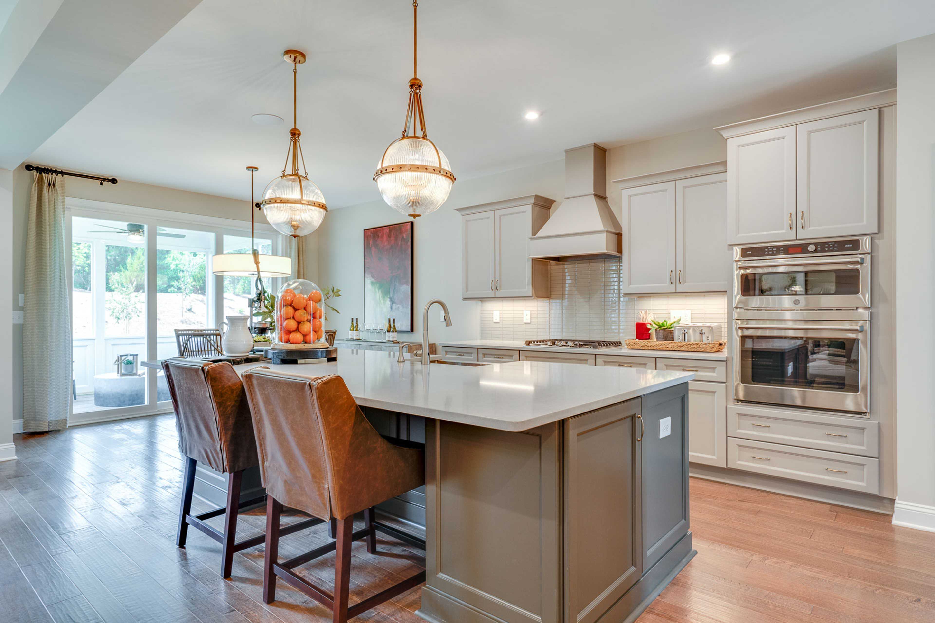 Spacious modern kitchen in Hasentree Wake Forest NC by Davidson Homes with white shaker cabinets, quartz island, leather bar stools, and gold pendant lights