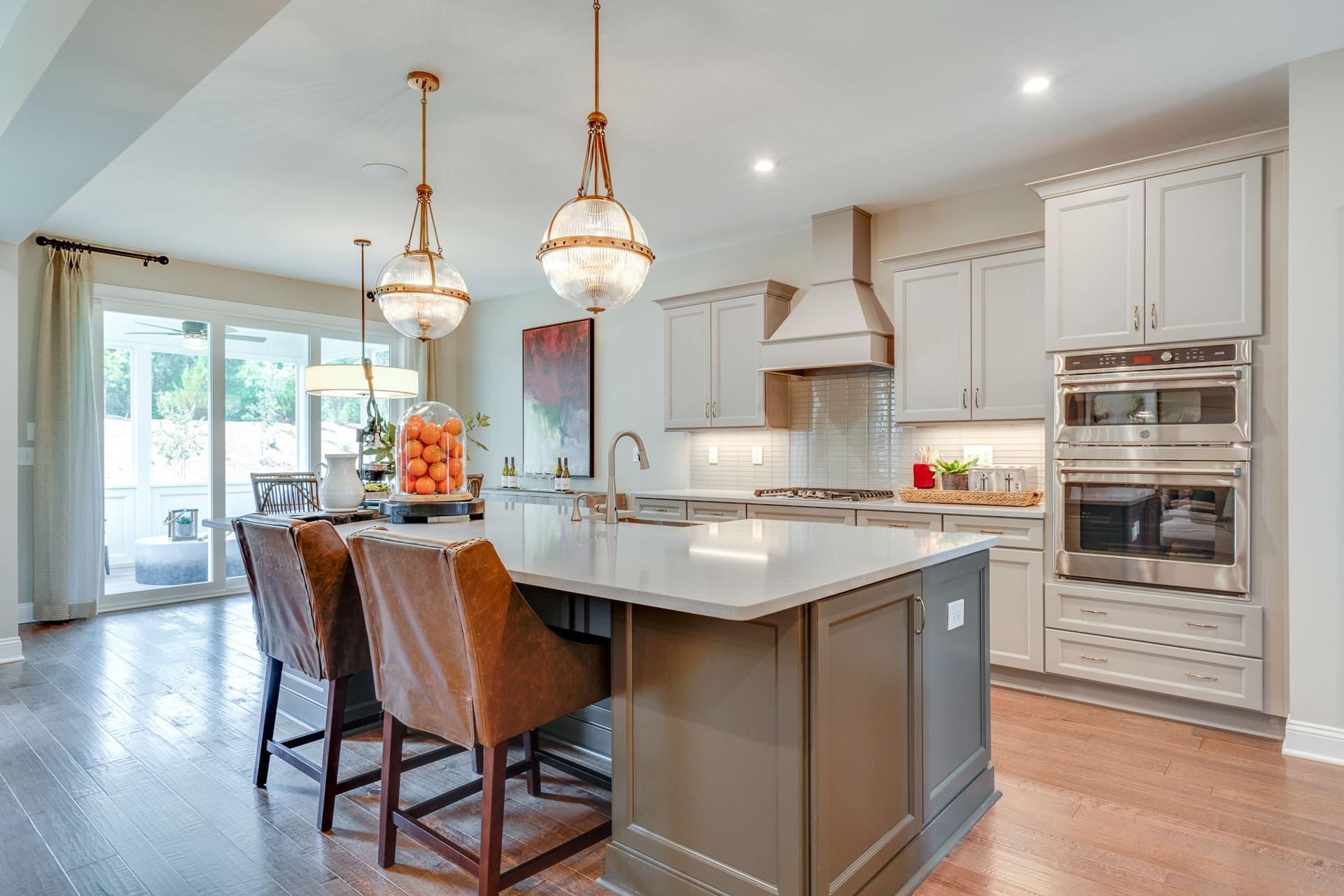 Spacious modern kitchen in Hasentree Wake Forest NC by Davidson Homes with white shaker cabinets, quartz island, leather bar stools, and gold pendant lights