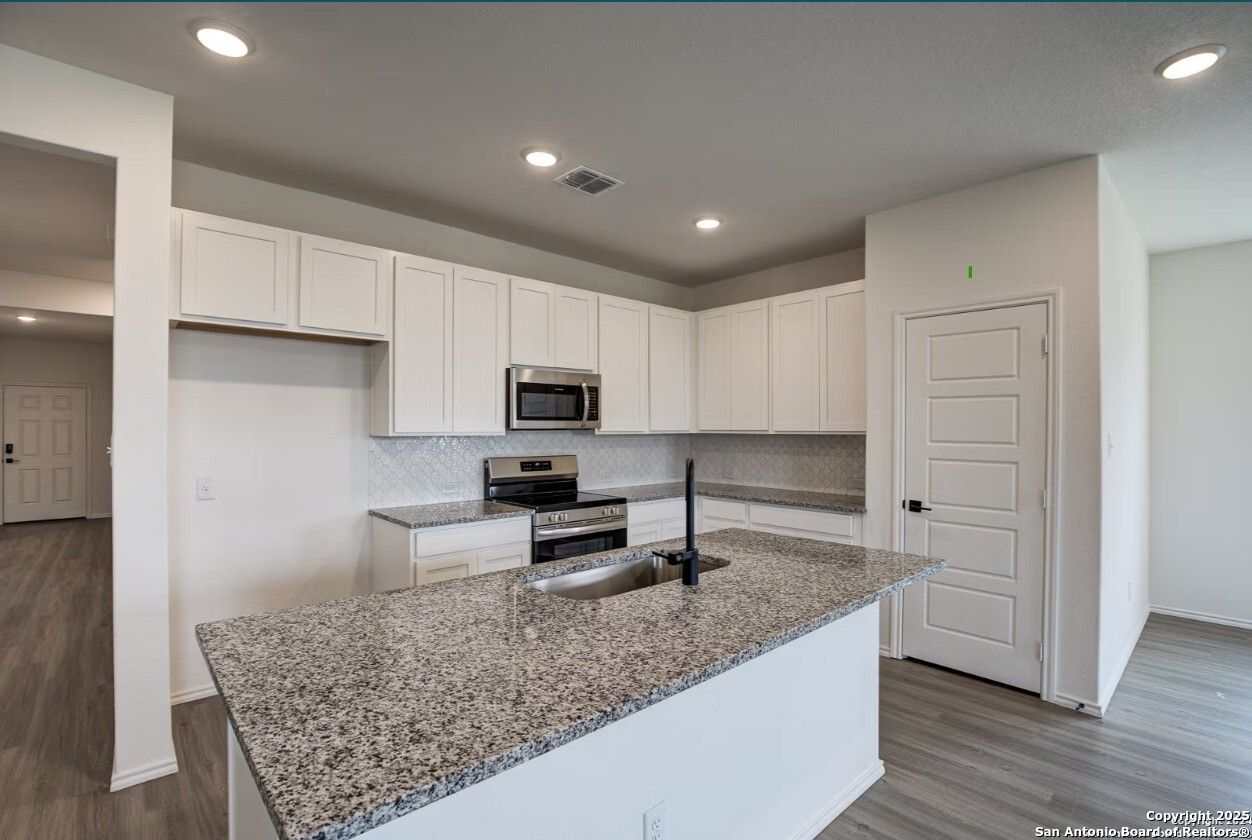 Modern white kitchen with granite island sink, stainless steel appliances, subway tile backsplash in The Daphne H, Seguin, TX