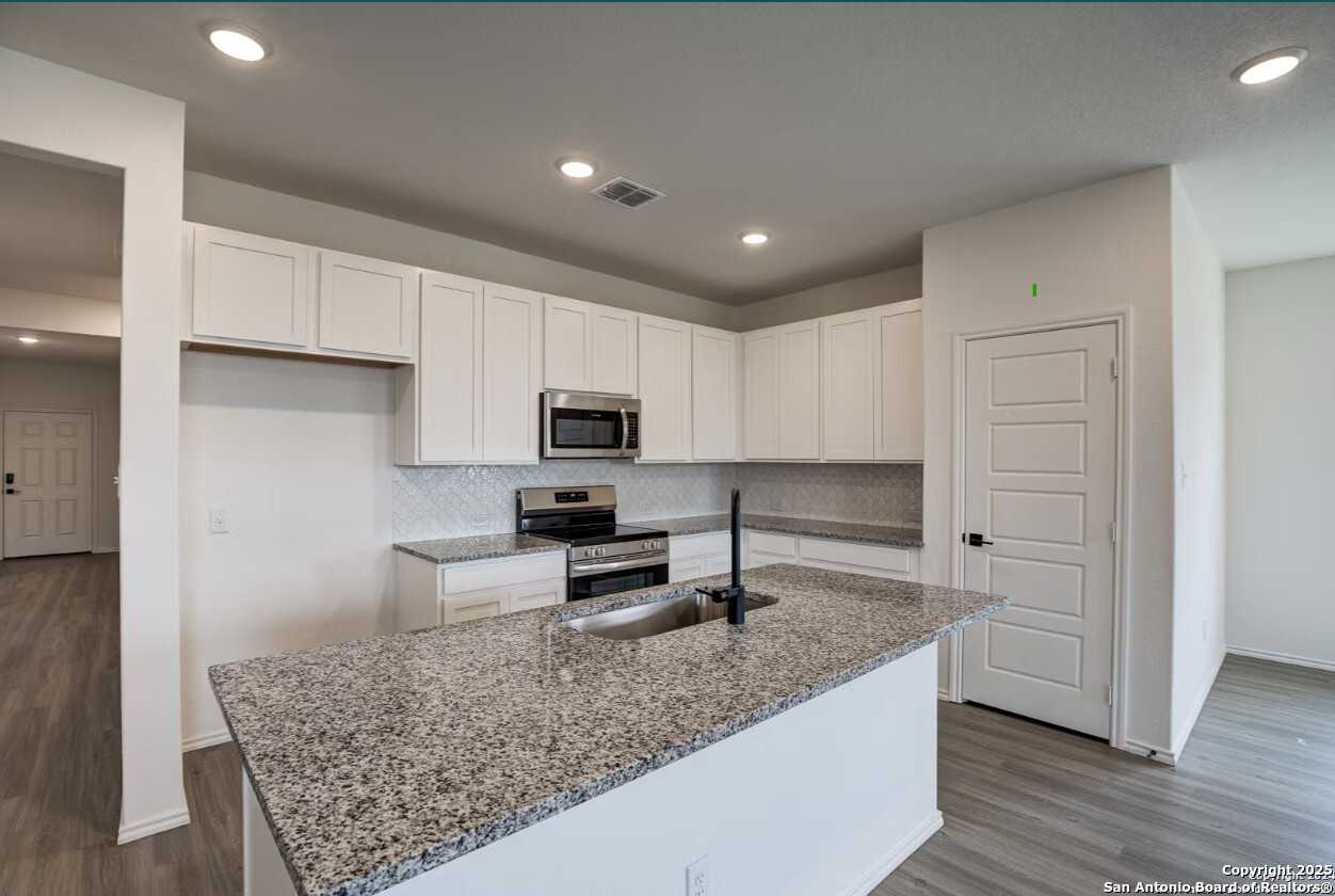 Modern white kitchen with granite island sink, stainless steel appliances, subway tile backsplash in The Daphne H, Seguin, TX