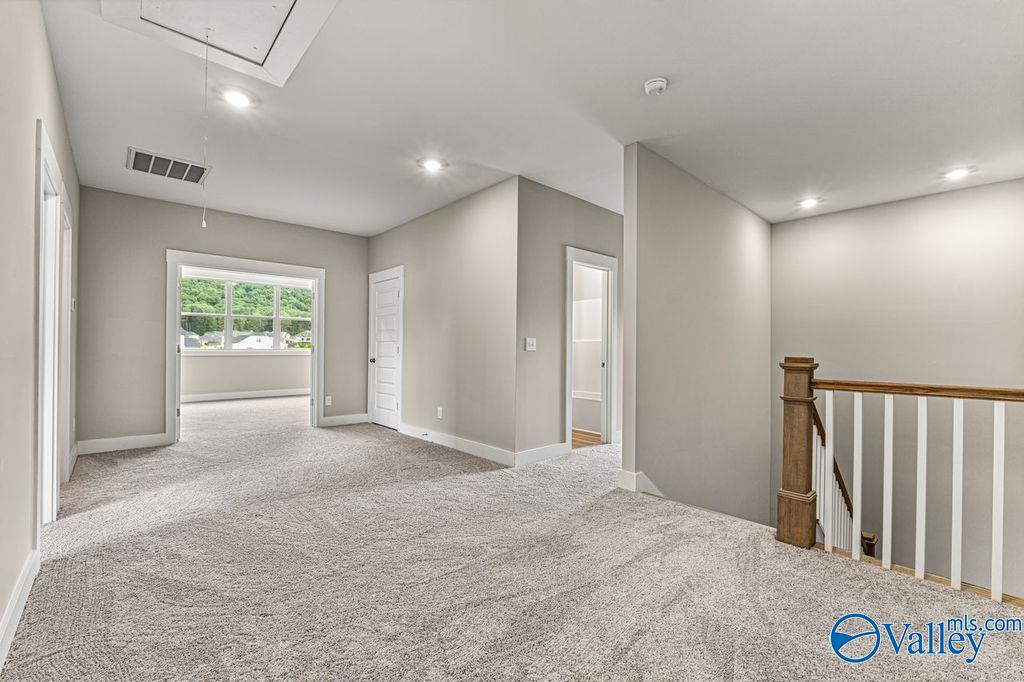 Spacious upstairs hallway with carpeted floors, beige walls, wooden balustrade, and large windows in Evermore Homes The Oxford, Owens Cross Roads, Alabama